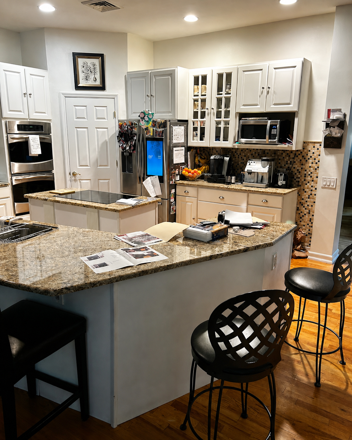 Modern kitchen with granite island, white cabinets, black stools, and hardwood floors