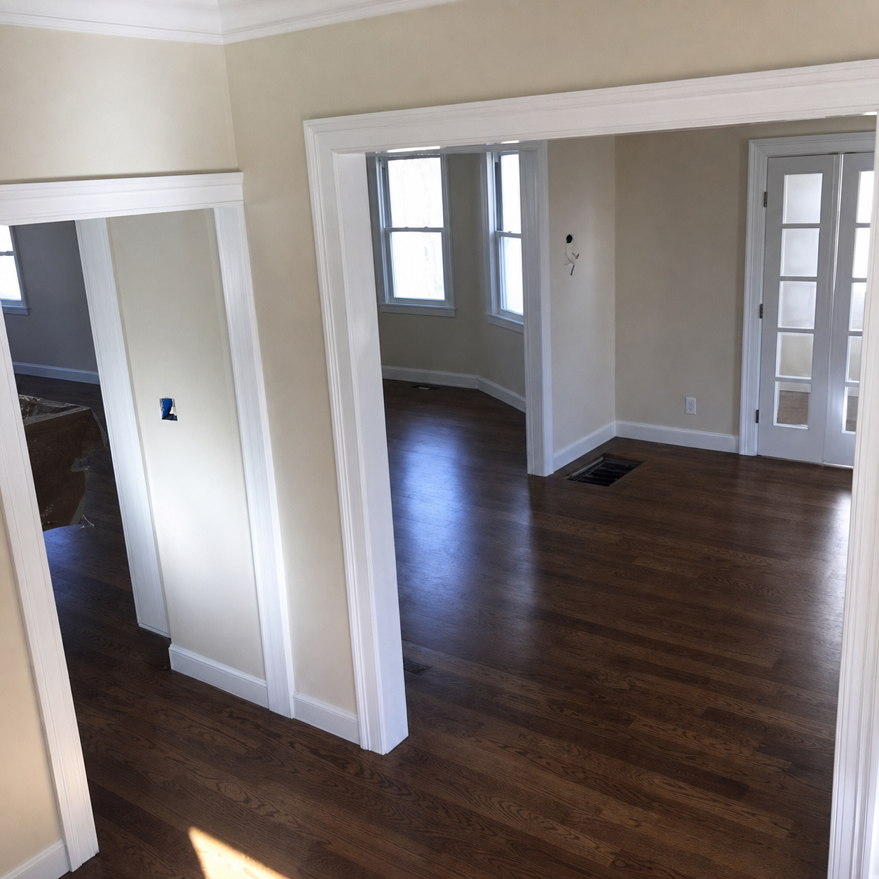 Empty living room with dark wood floors, white trim, and large openings to adjacent rooms