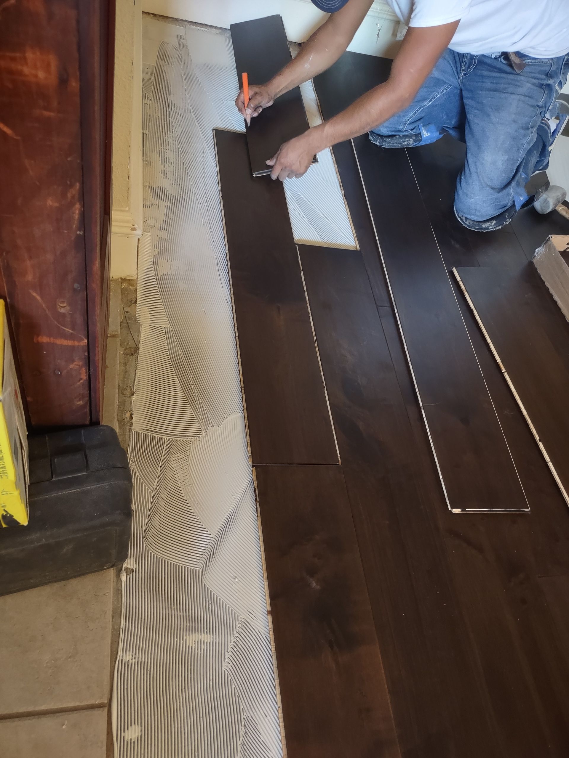 Person installing underlayment on dark wood flooring beside a patterned rug, using a tool.