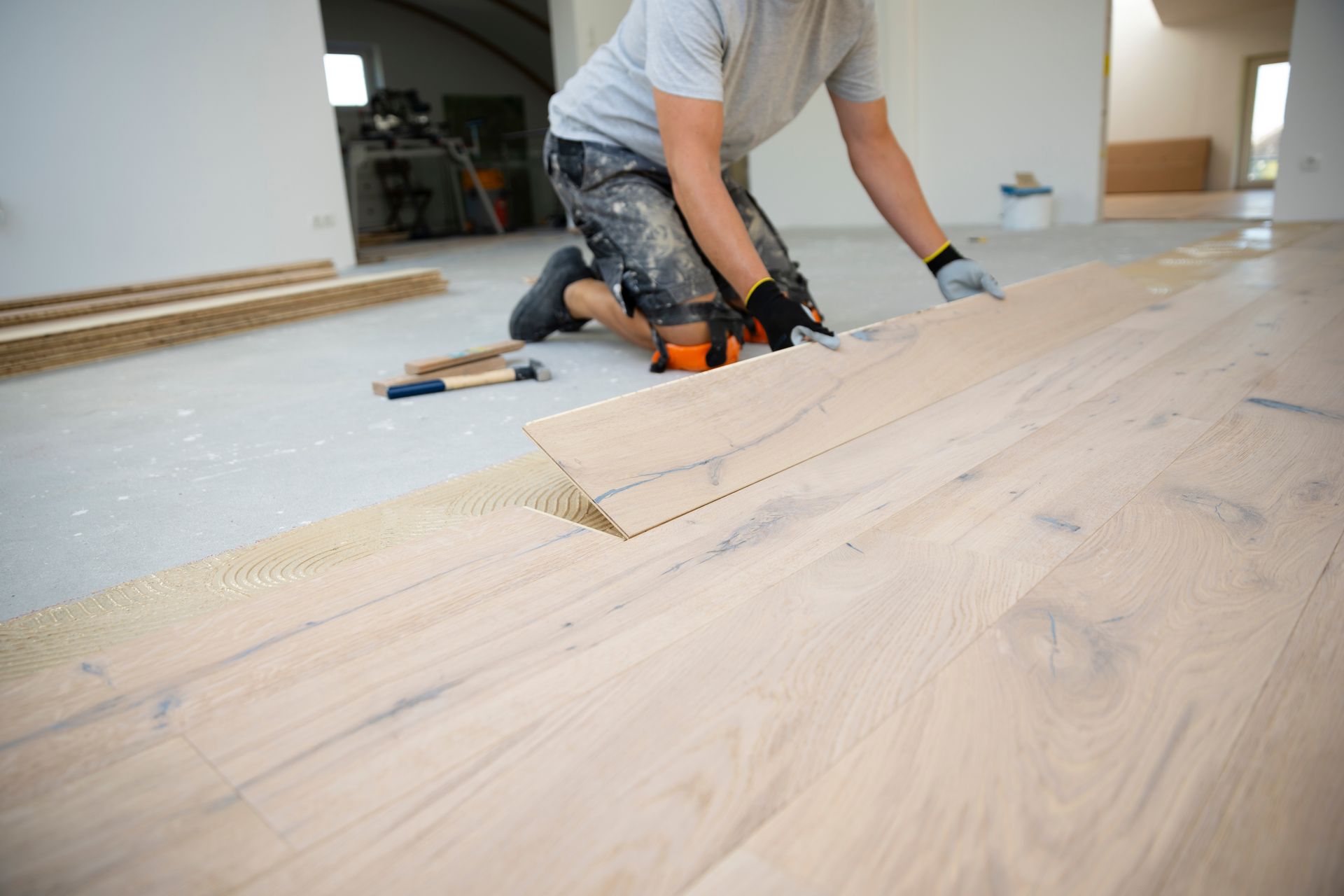 Person installing light wood flooring with a power tool in an unfinished room