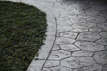Curved concrete path beside green grass, with a cracked stone surface