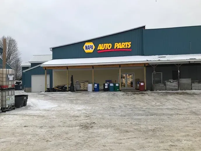 A napa auto parts store in the snow with a truck parked in front of it.