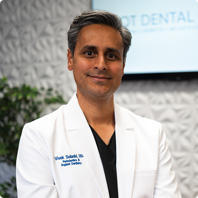 Smiling doctor in a white coat stands in a dental office.