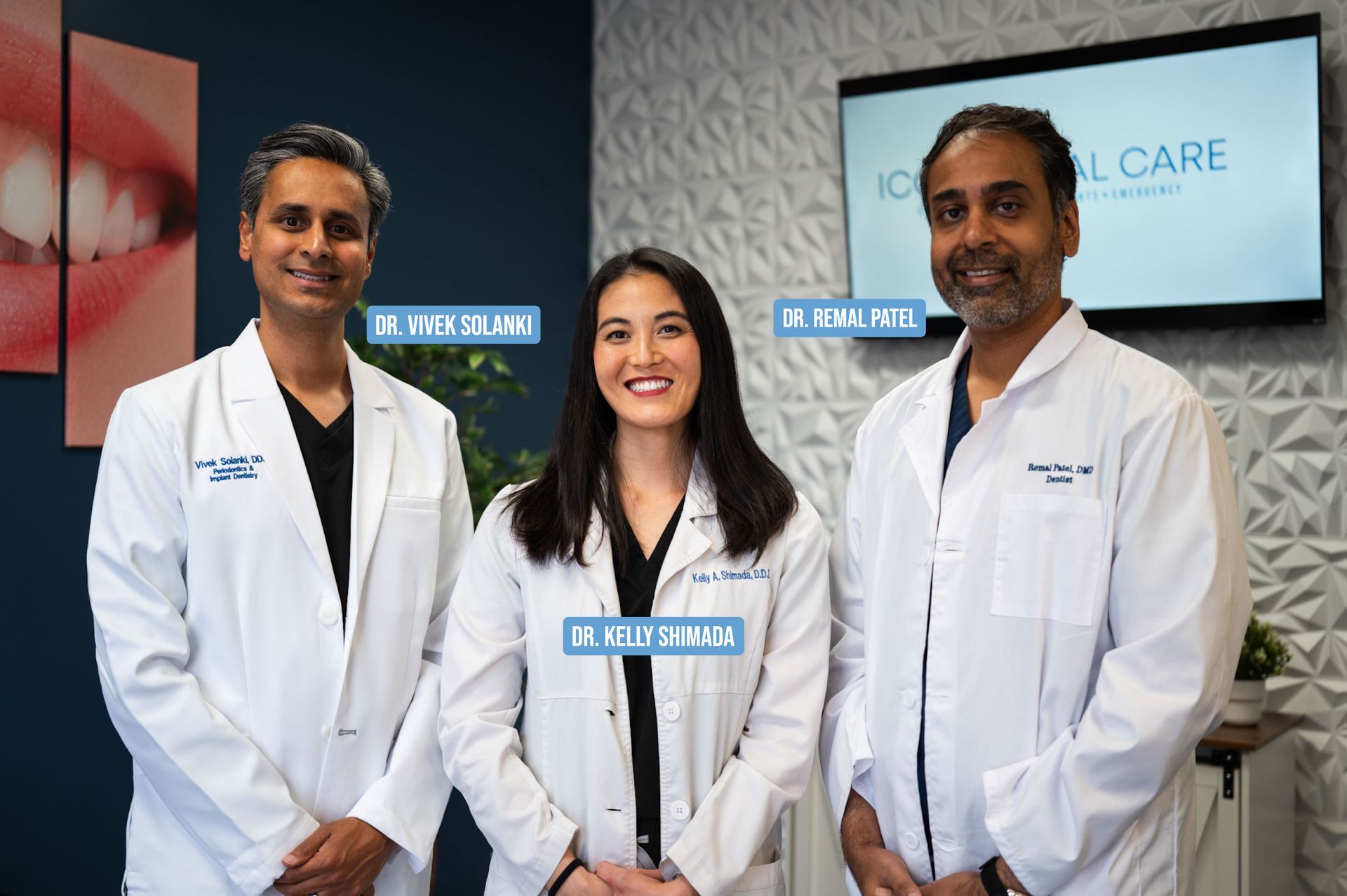 Three doctors in white coats, smiling in dental office.