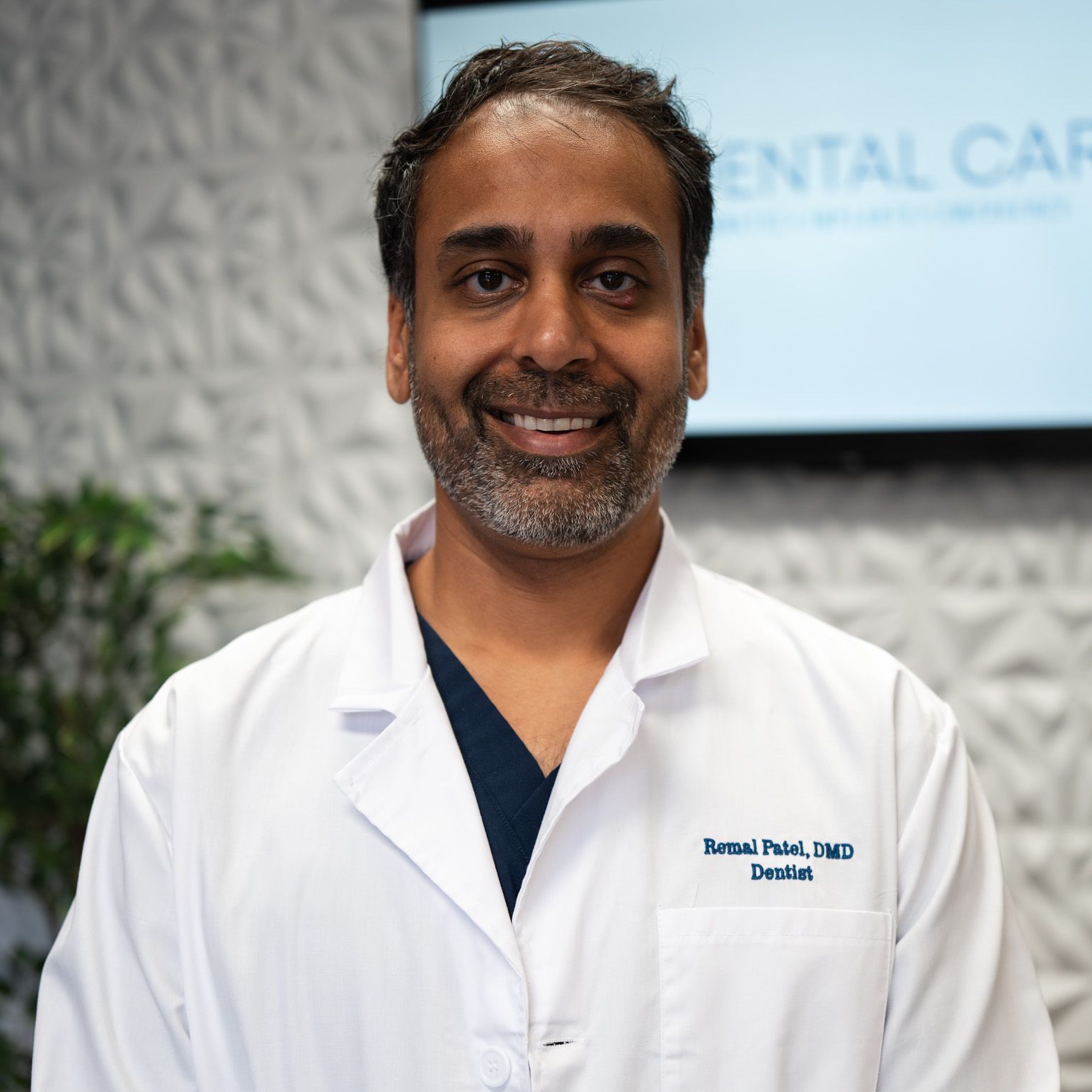 Man in a white coat smiling, standing in front of 