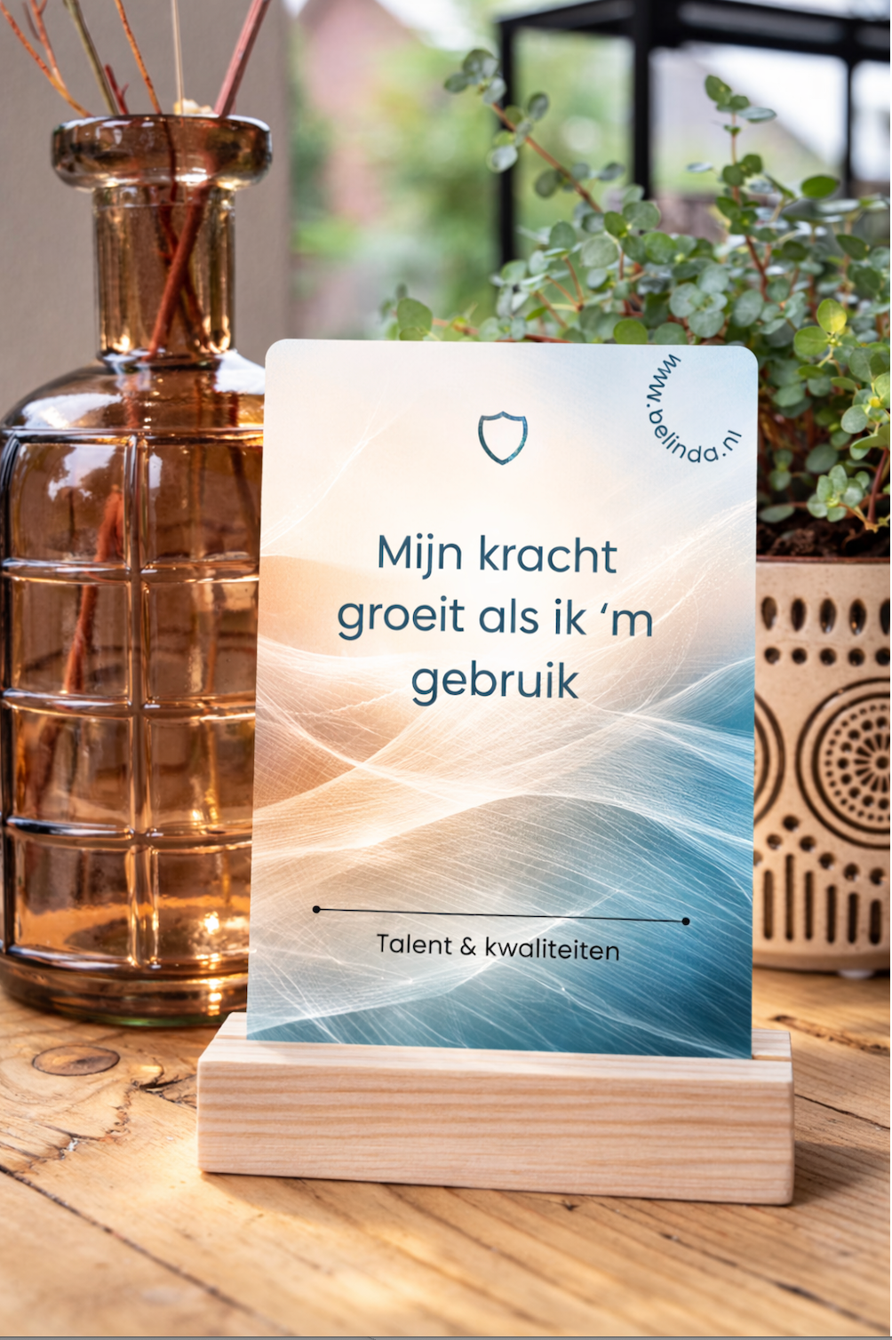 Witte kaart met Nederlandse tekst op houten standaard, naast glazen vaas en planten op een tafel