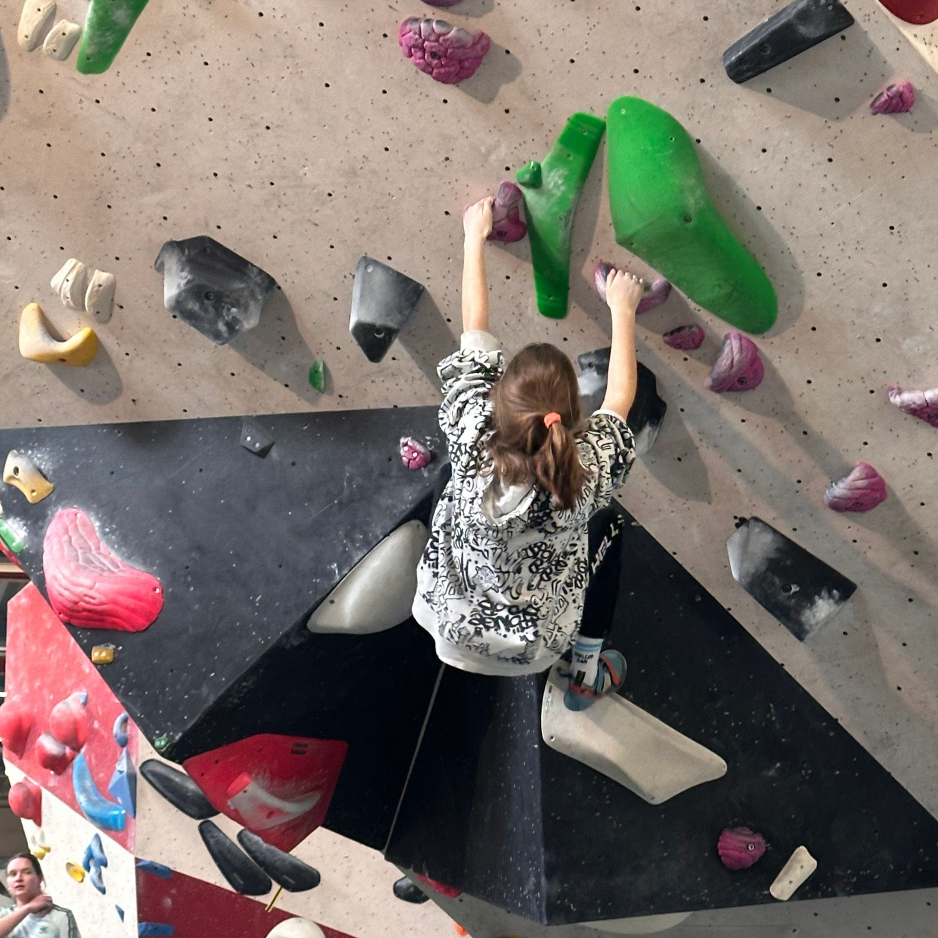 Kind klimt op een indoor boulderwand met groene en roze klimgrepen.
