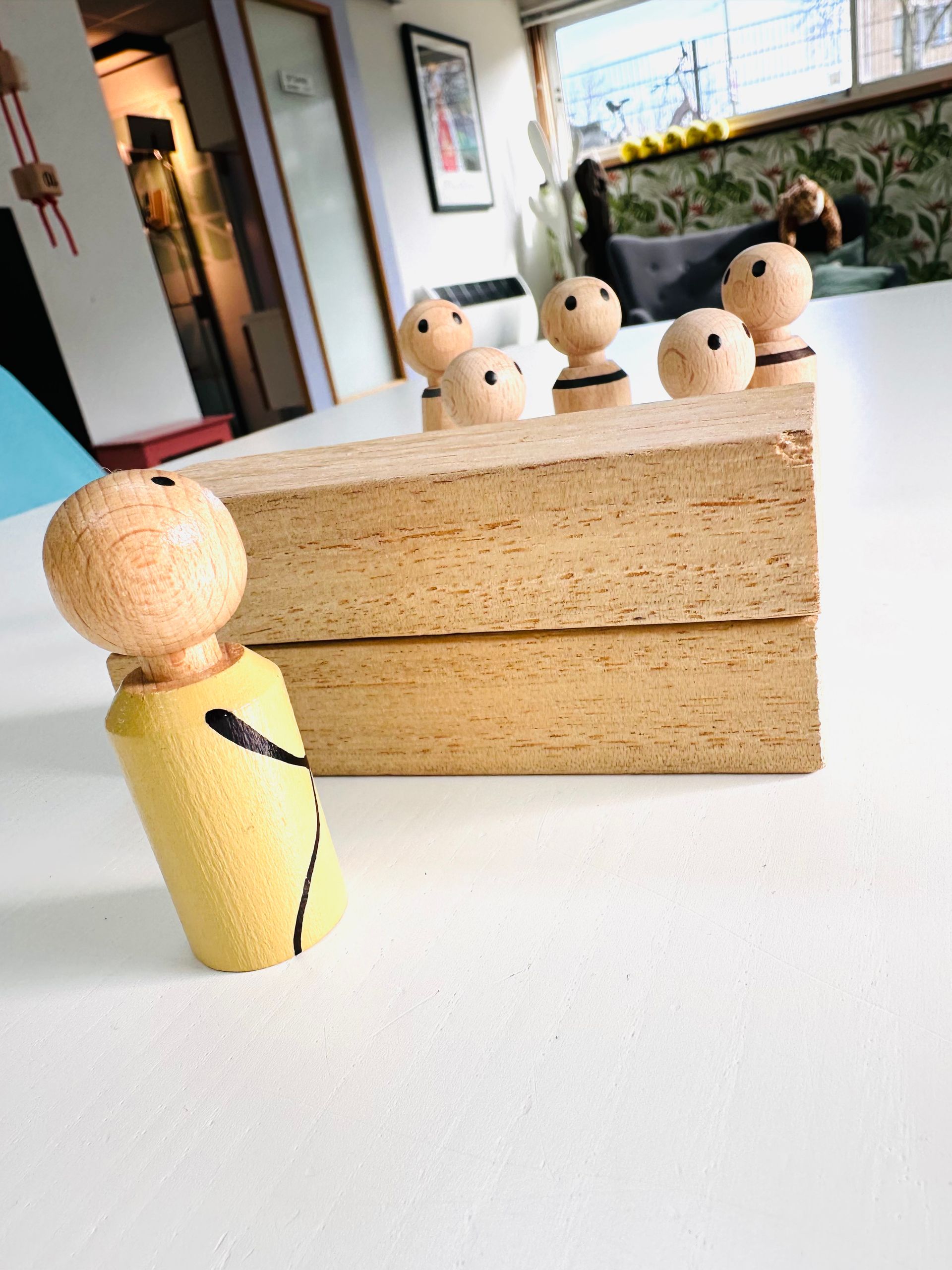 Houten poppetjes staan ​​opgesteld rond een klein houten blokje, met een geel poppetje op de voorgrond.
