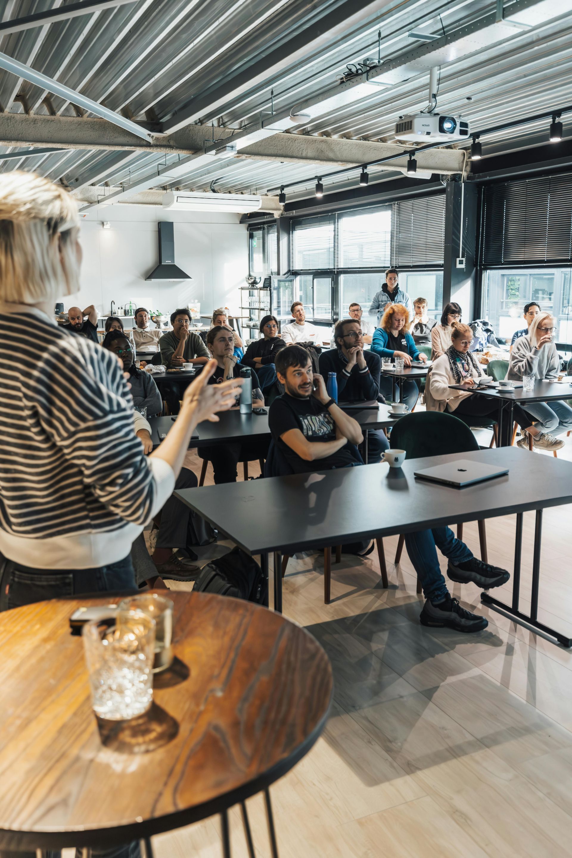 Spreker spreekt zittend publiek toe in een lichte vergaderruimte in industriële stijl.