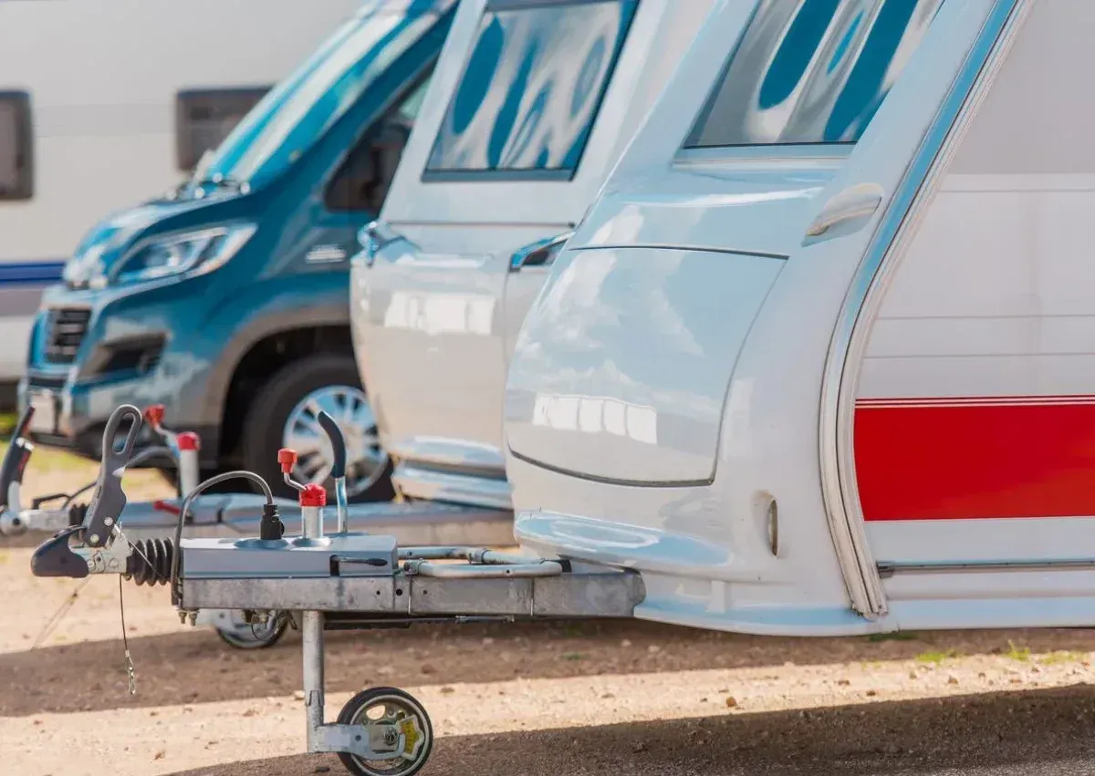 A trailer is parked in a gravel lot next to a row of camper vans.