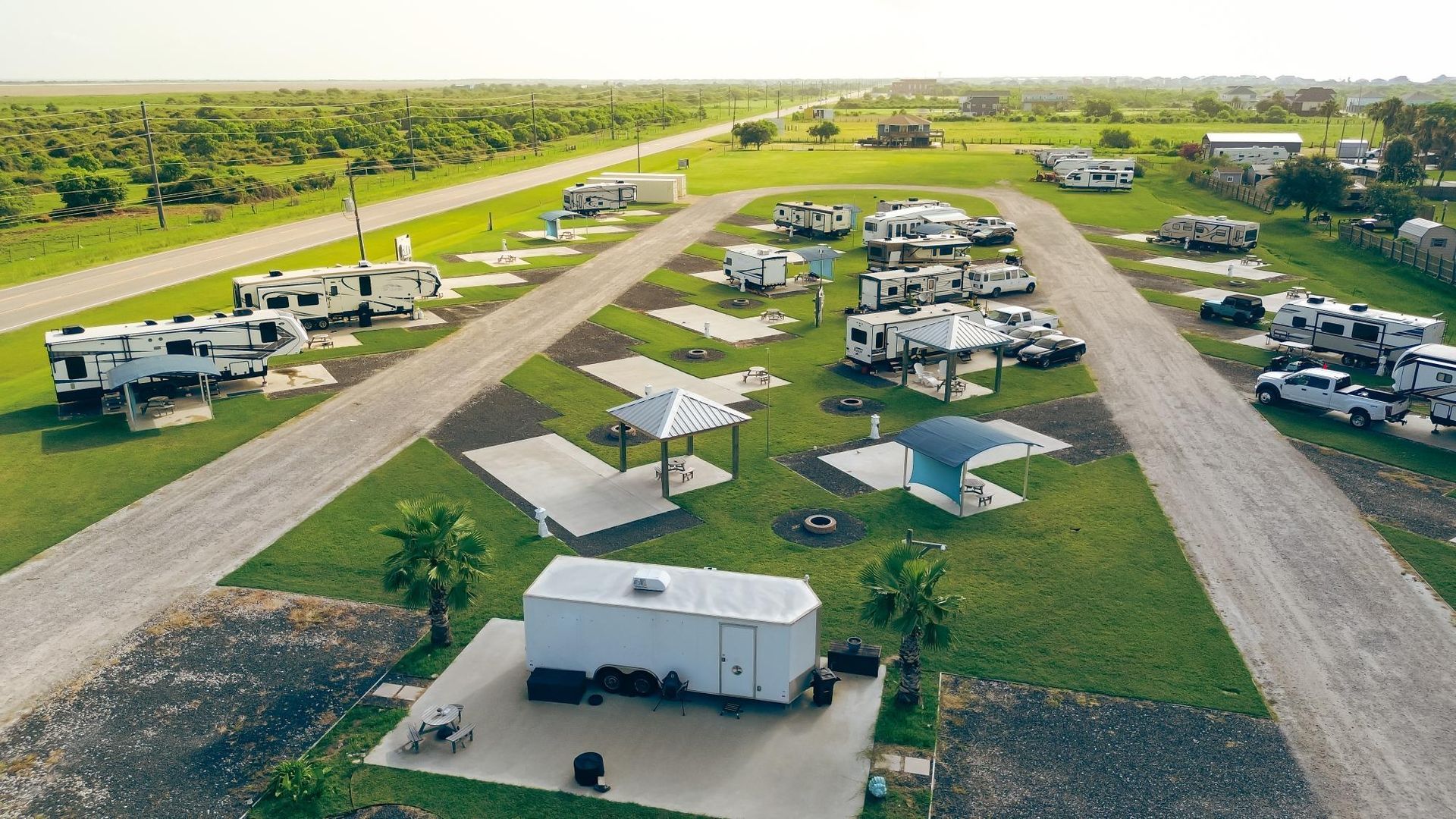 Aerial view of an RV park with various RVs parked on gravel sites. Green grass and trees surround.