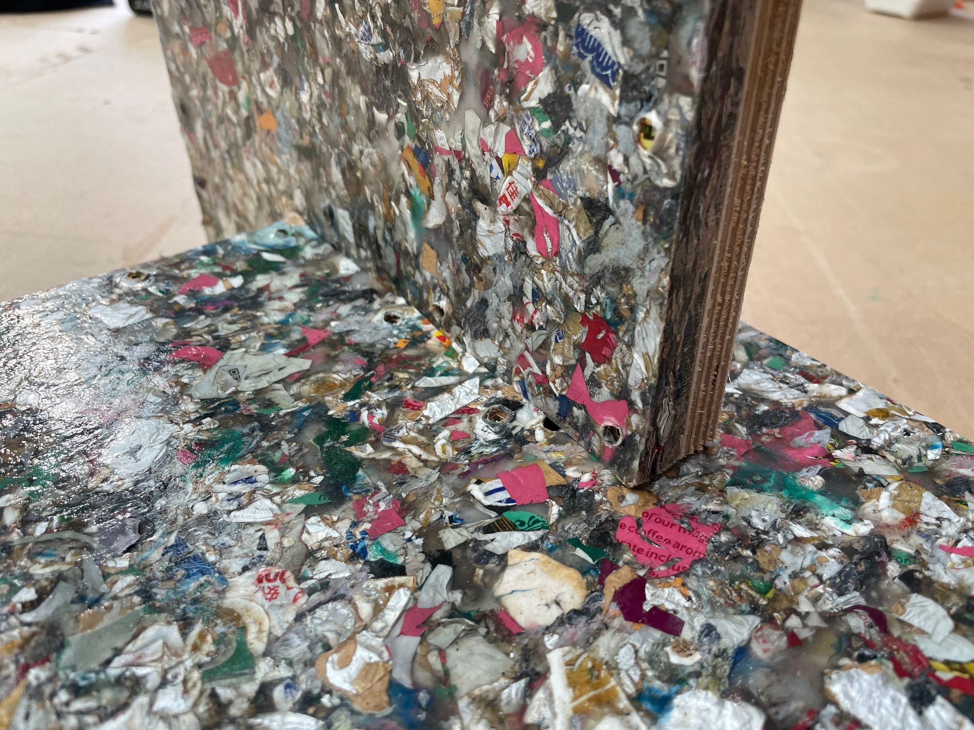 Close-up of a saveBOARD material block, made of recycled plastic pieces, resting on another similar block.