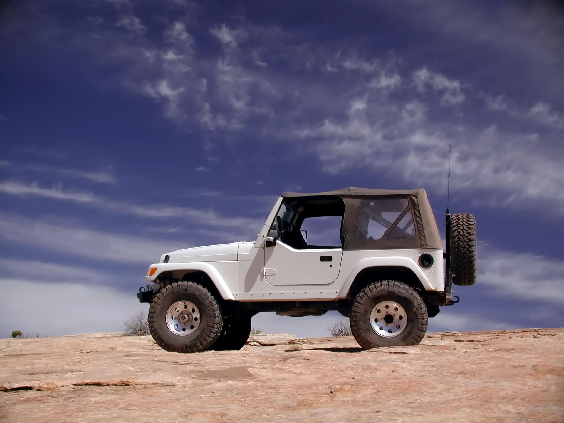A white jeep is parked on top of a rocky hill.