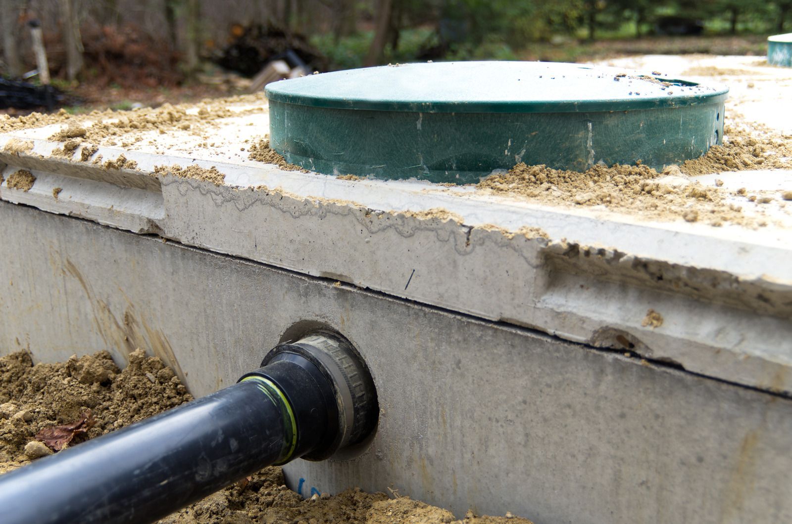A septic tank with a green lid and a black pipe coming out of it.