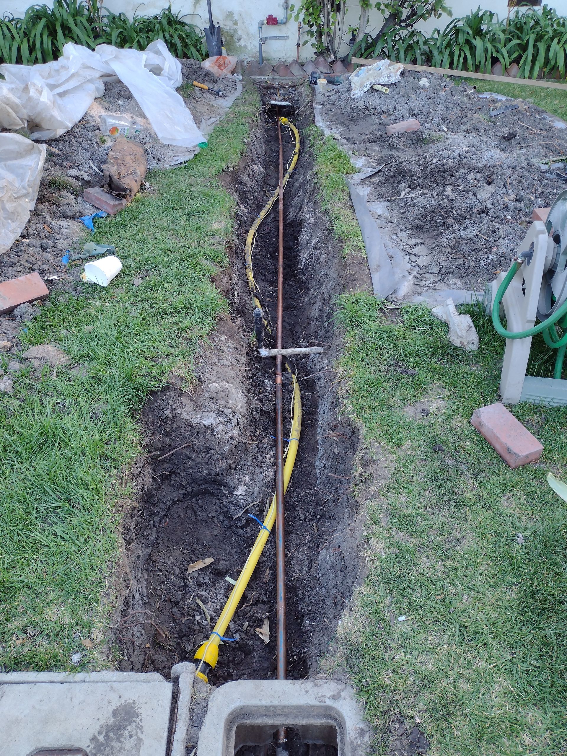 A yellow hose is being installed in a trench in a yard.