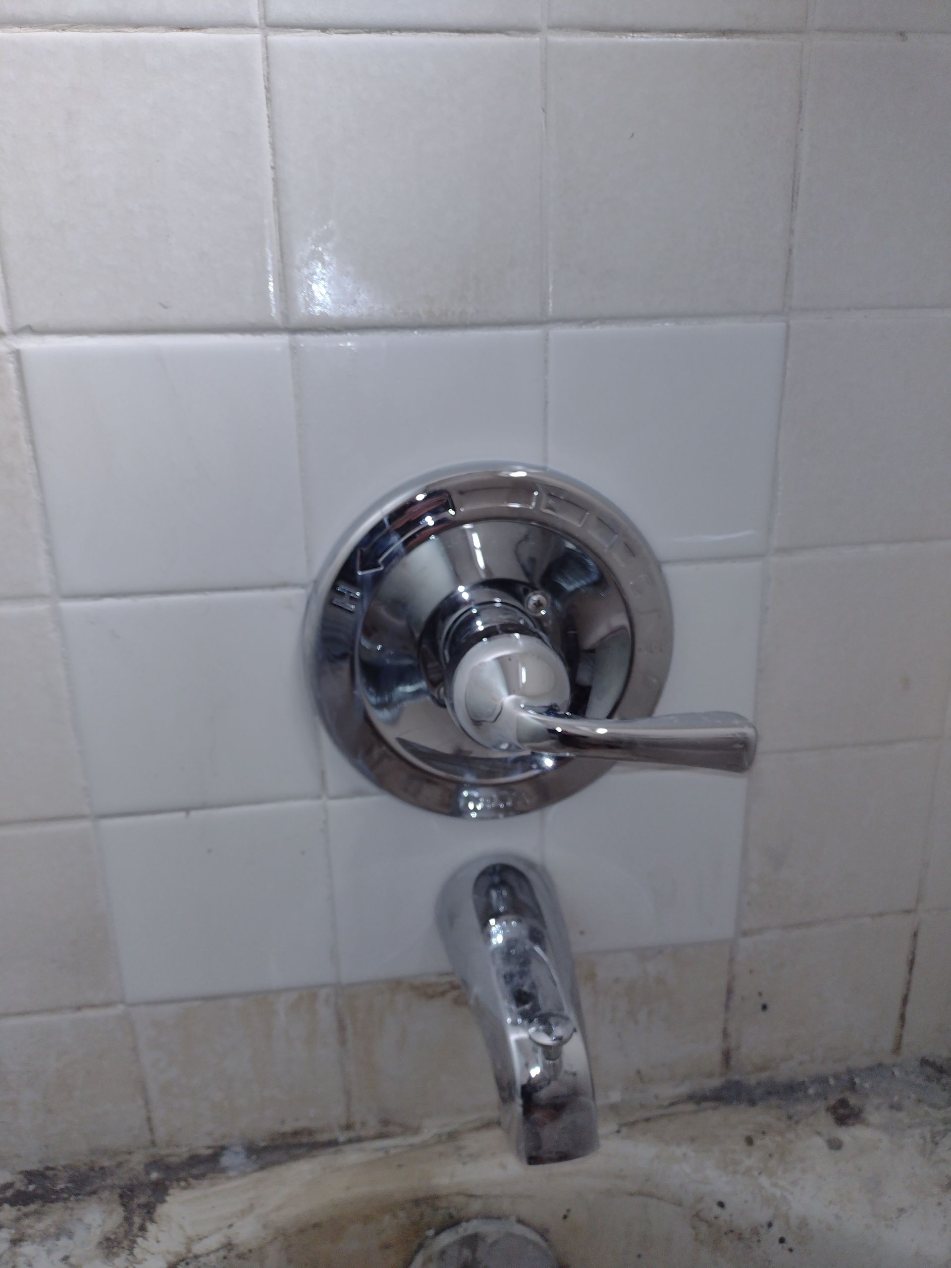 A close up of a bathtub faucet on a tiled wall.