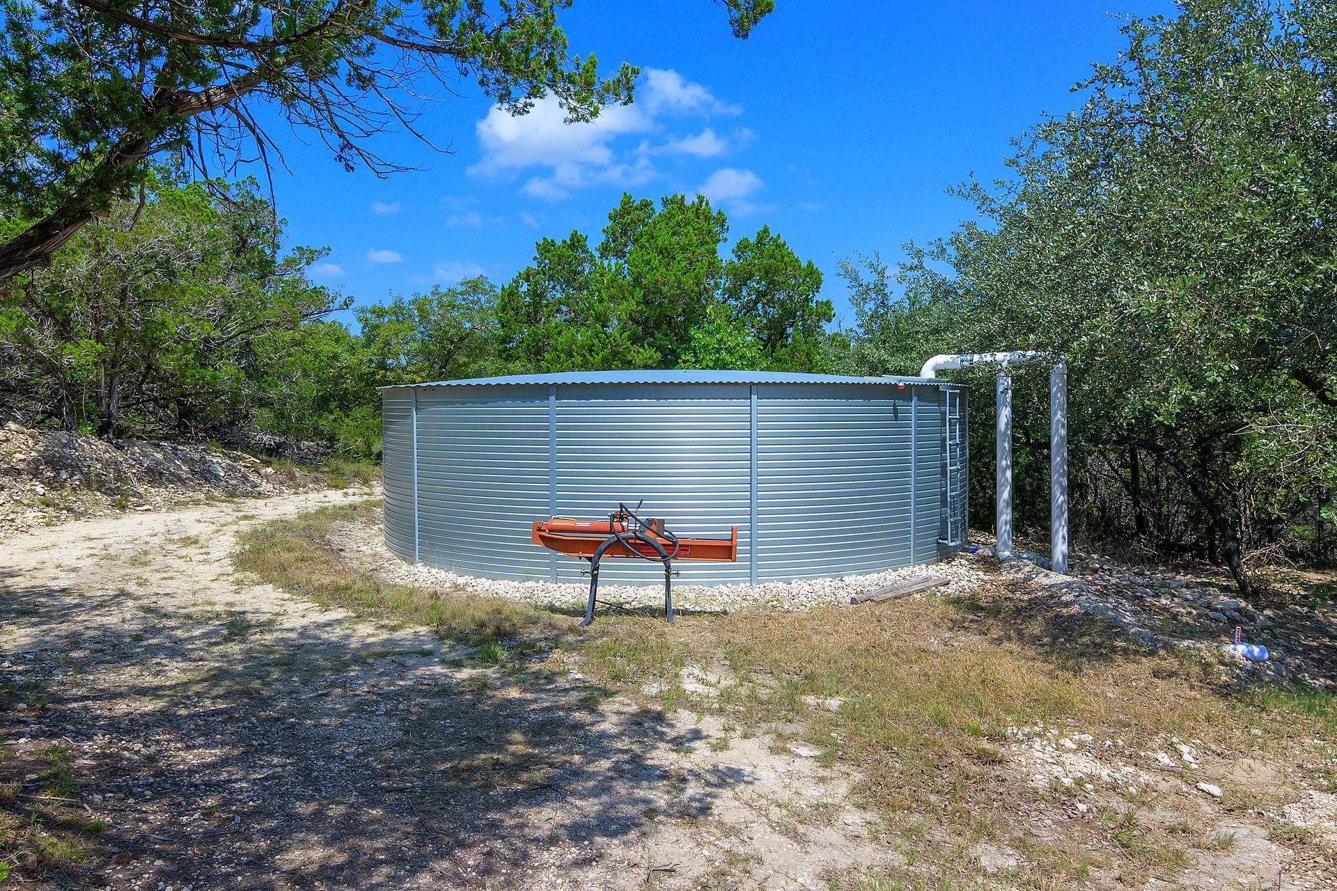 A large metal water tank is sitting in the middle of a dirt field.
