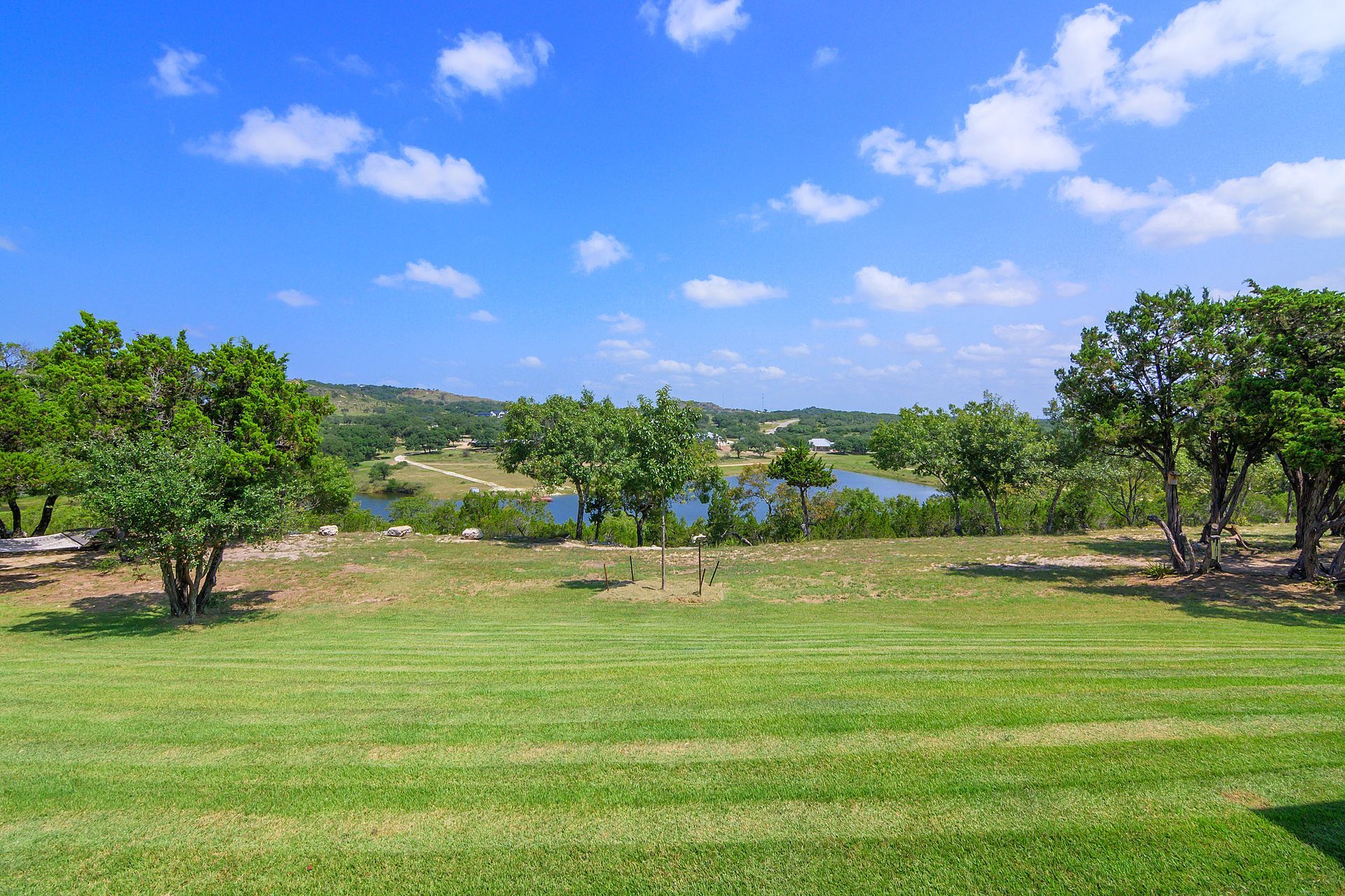 A large lush green field with trees and a lake in the background on a sunny day.