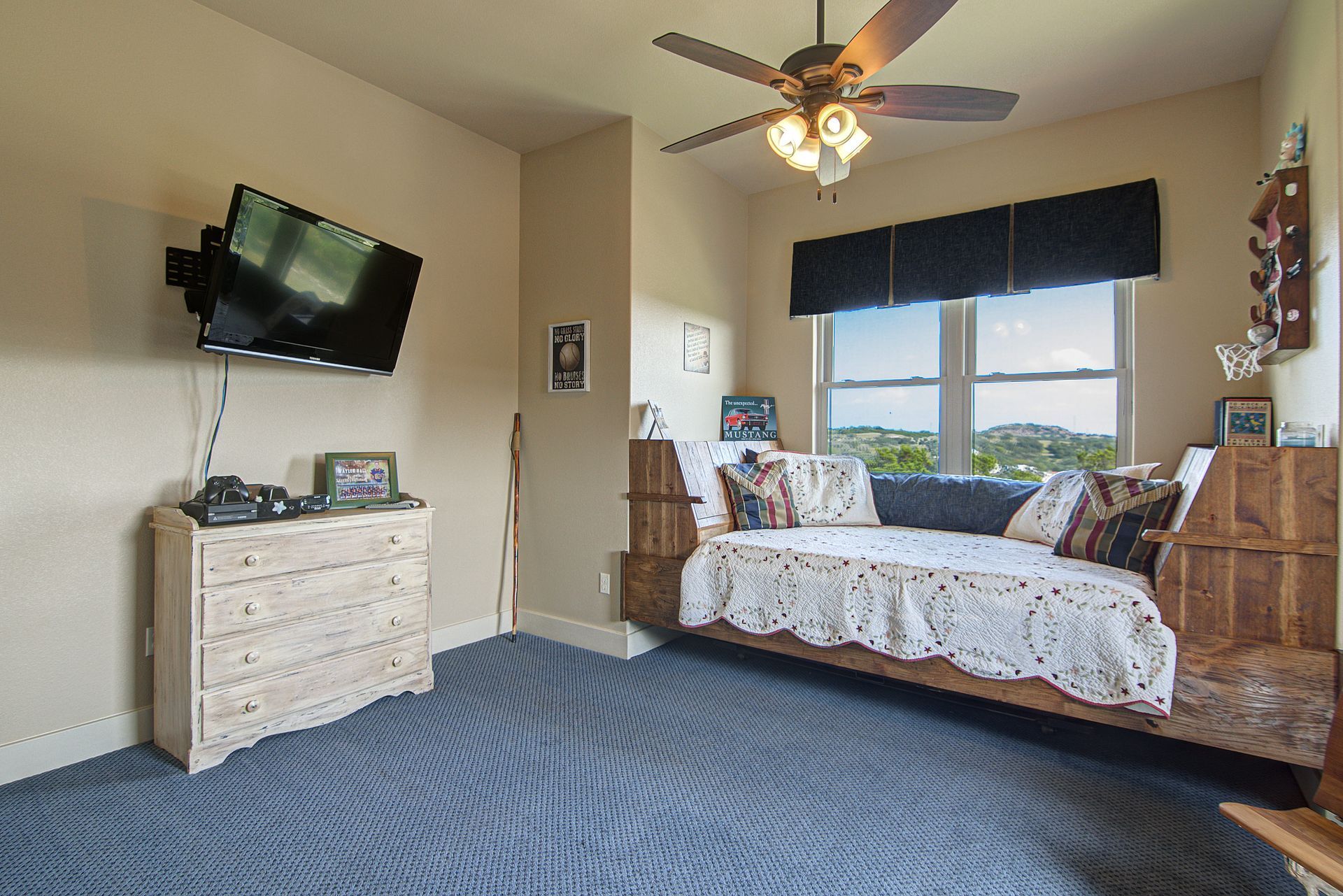 A bedroom with a day bed , dresser , television and ceiling fan.