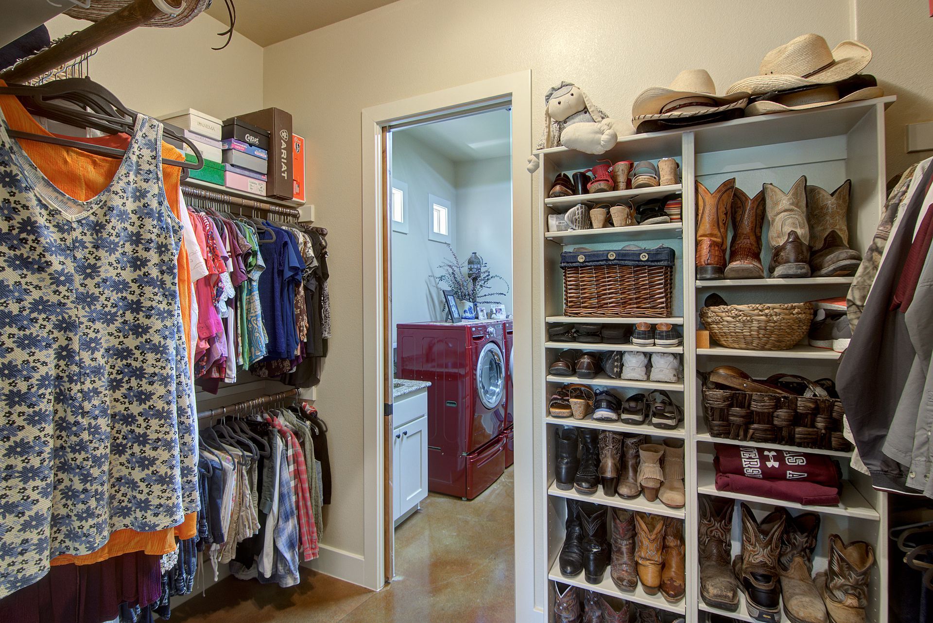 A walk in closet with a laundry room in the background.