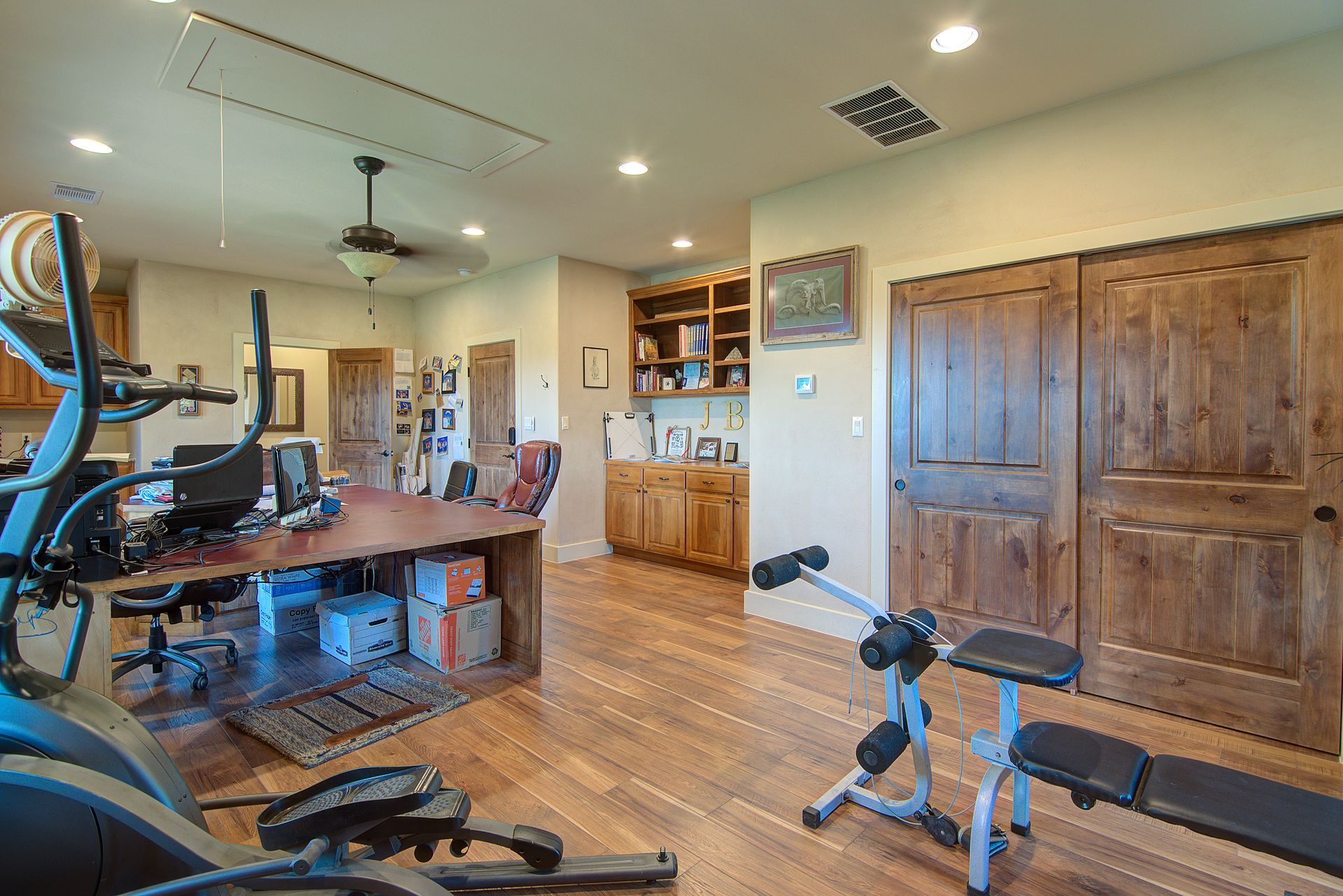 A home office with a desk , exercise bike , and a bench.