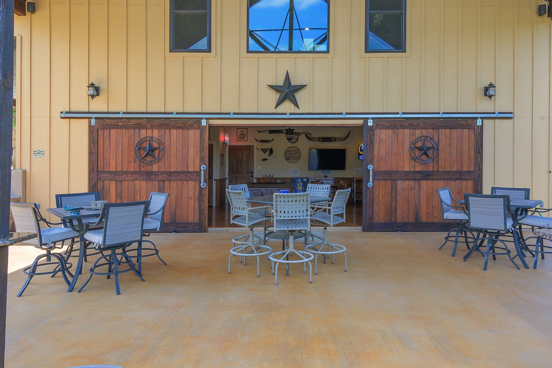 A patio with tables and chairs in front of a building with sliding barn doors.
