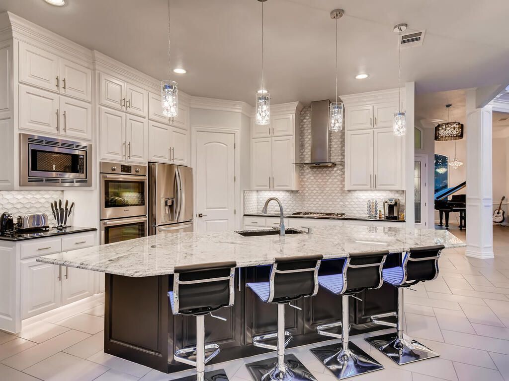 A kitchen with white cabinets , granite counter tops , stainless steel appliances and a large island.