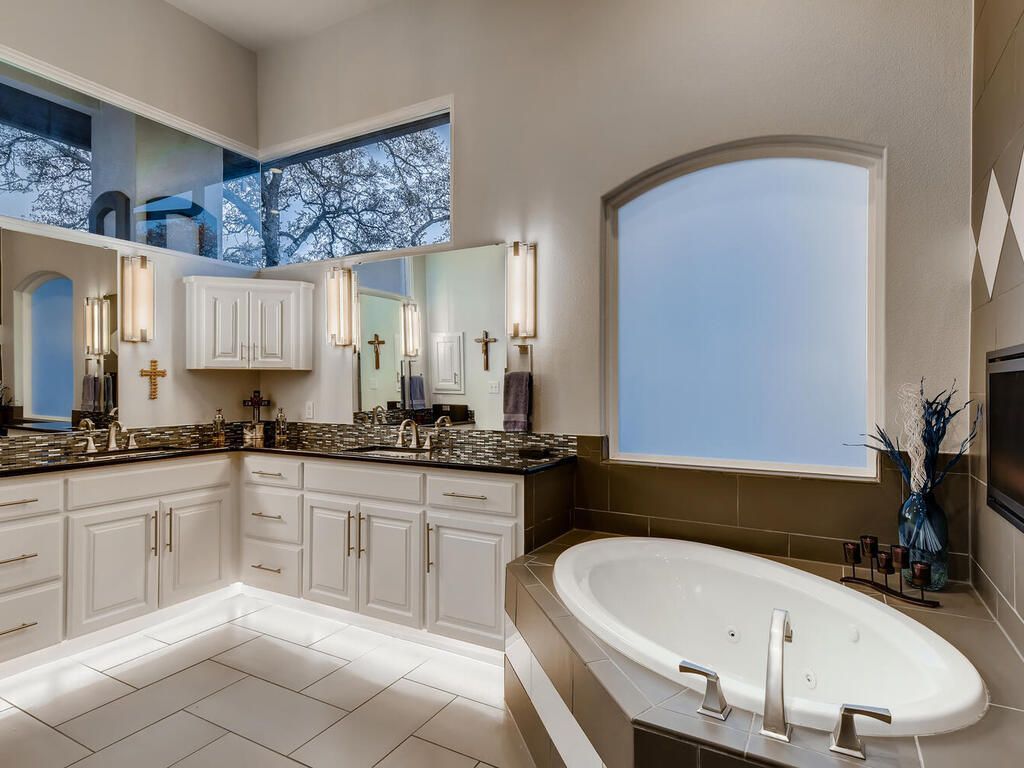 A bathroom with two sinks , a tub , and a large window.