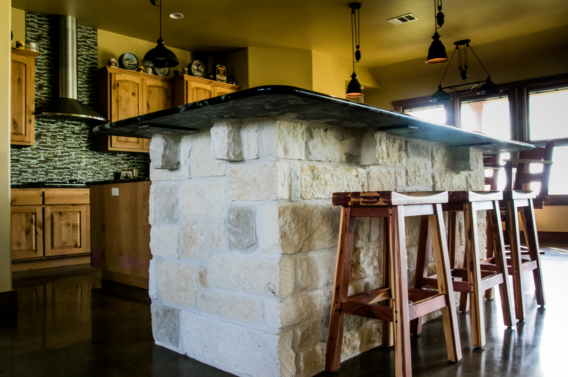 A kitchen with a stone island and wooden stools