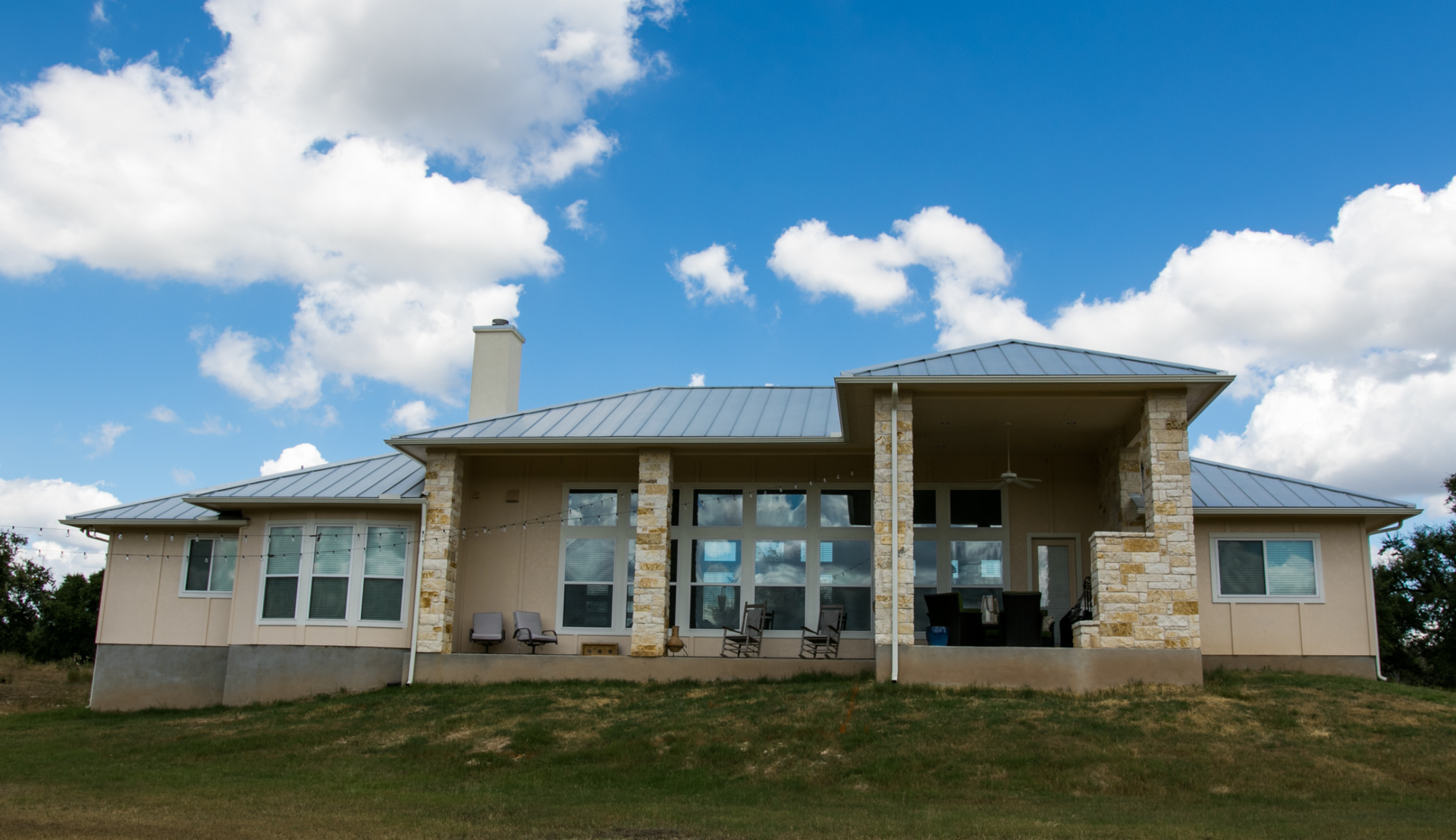 A large house with a metal roof is sitting on top of a grassy hill.