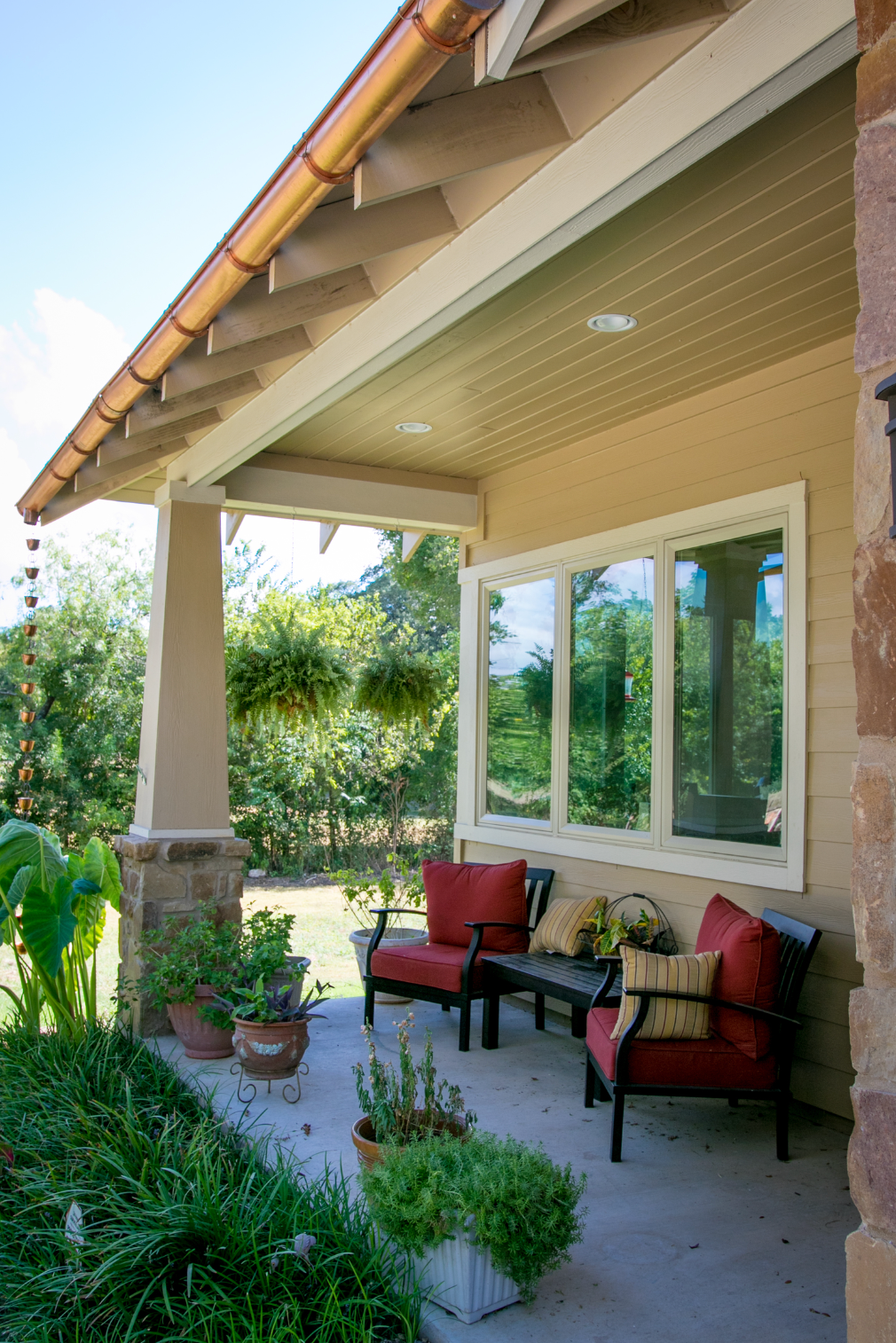 A porch with chairs , a table , and potted plants.