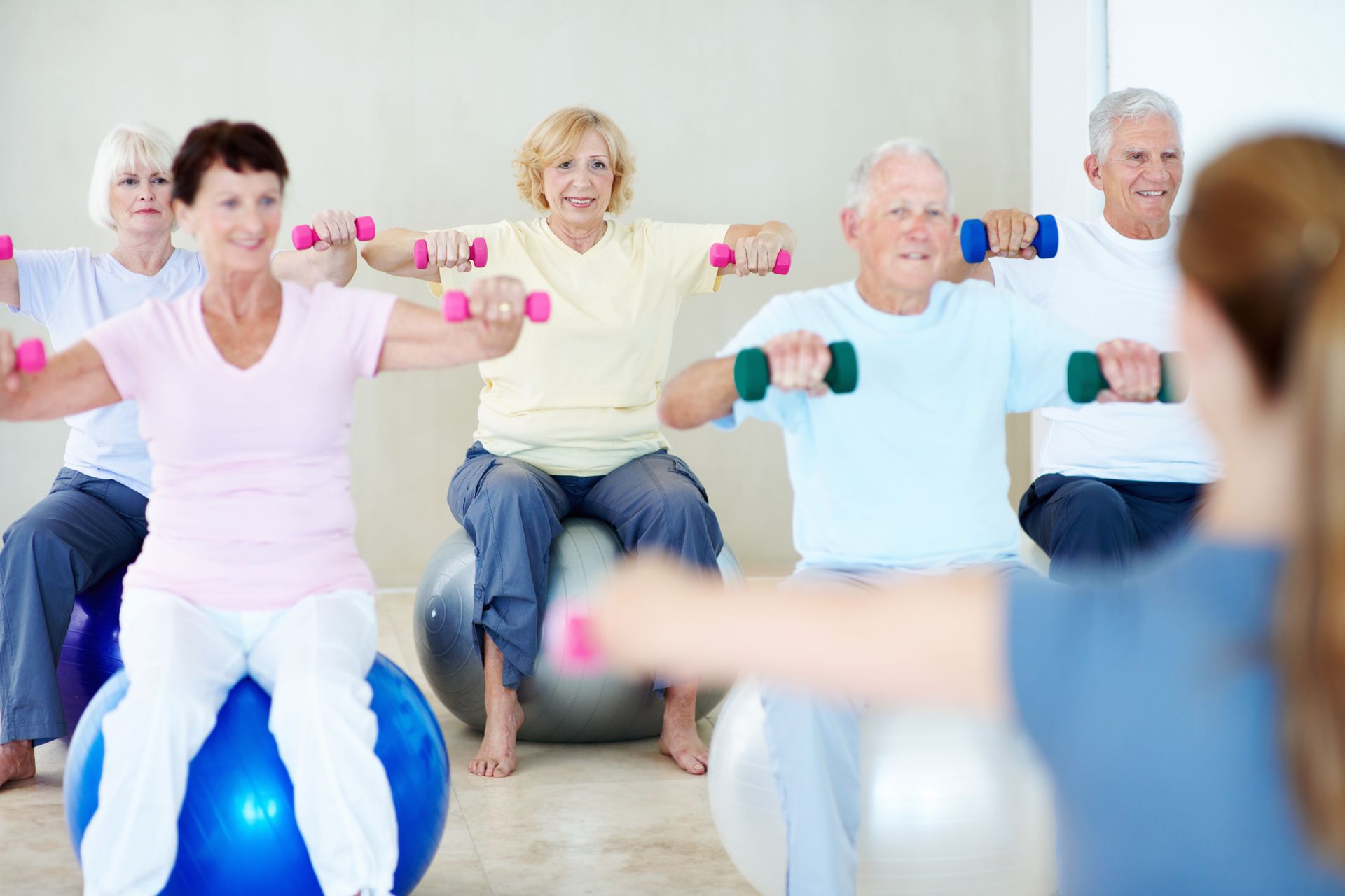 Un gruppo di anziani è seduto su palle da ginnastica e solleva manubri.