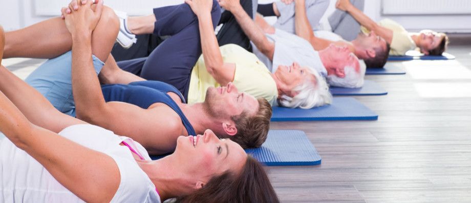 Un gruppo di persone è sdraiato a pancia in giù su tappetini da yoga in una palestra.