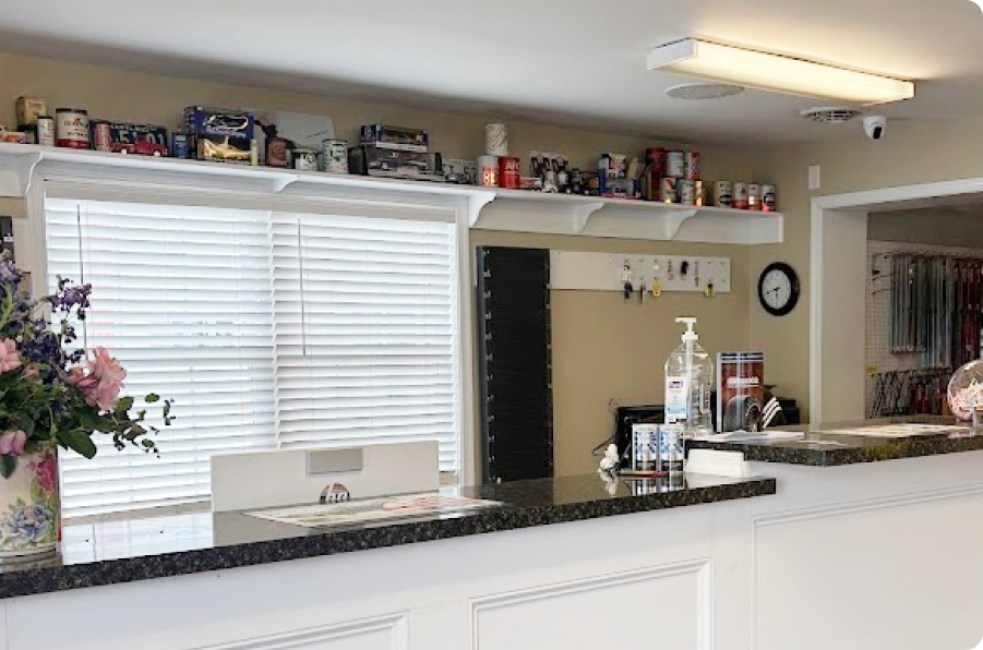 Clean reception desk with granite counter, shelves, wall clock, and window blinds in a bright lobby | Denton Auto Care And Tire