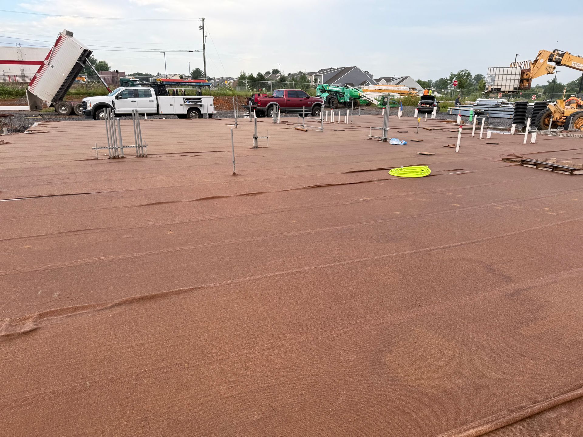 Large muddy lot with parked vehicles, scattered poles, and construction equipment under a cloudy sky