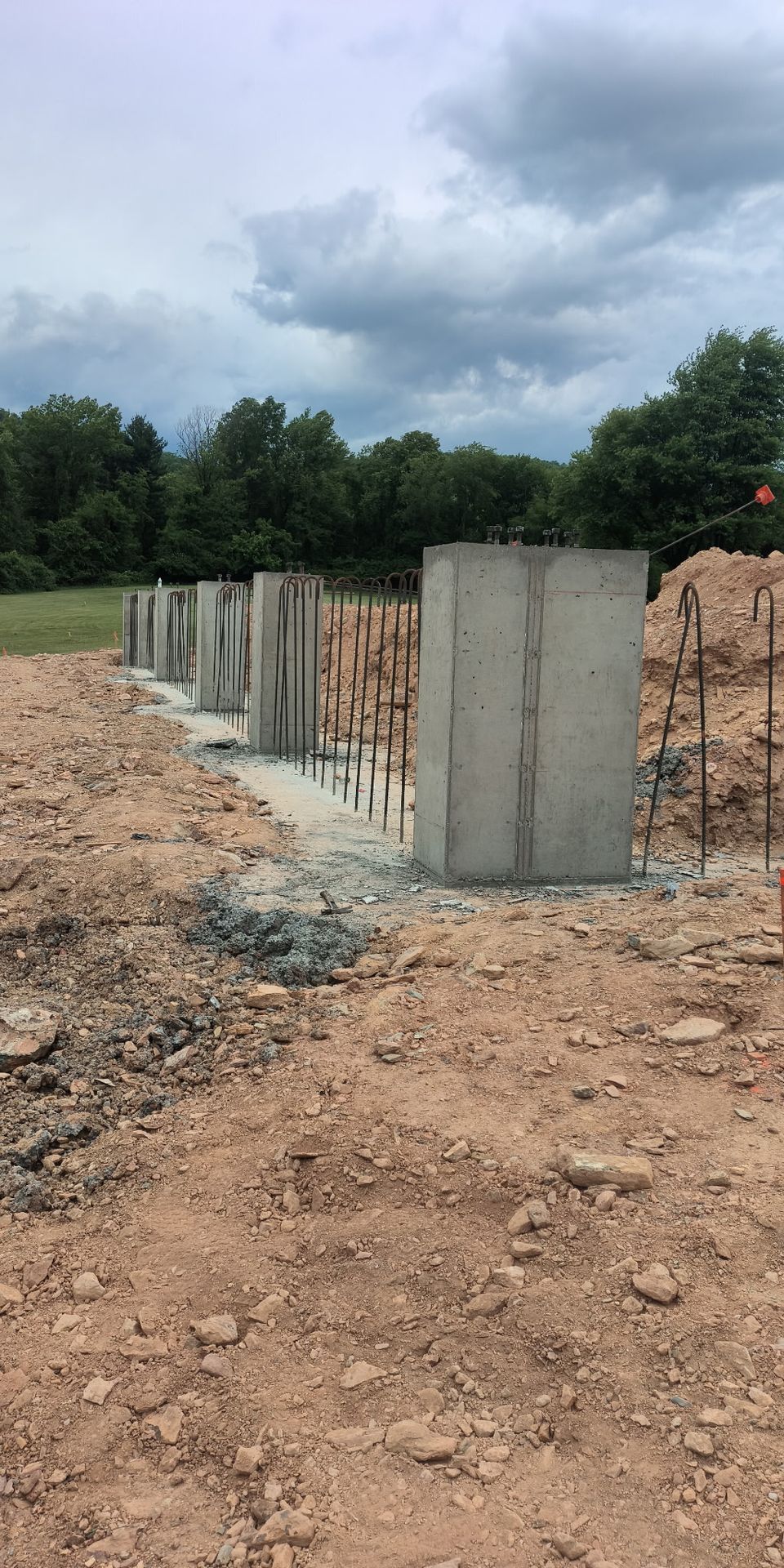 Partially built concrete wall on a dirt lot under cloudy sky