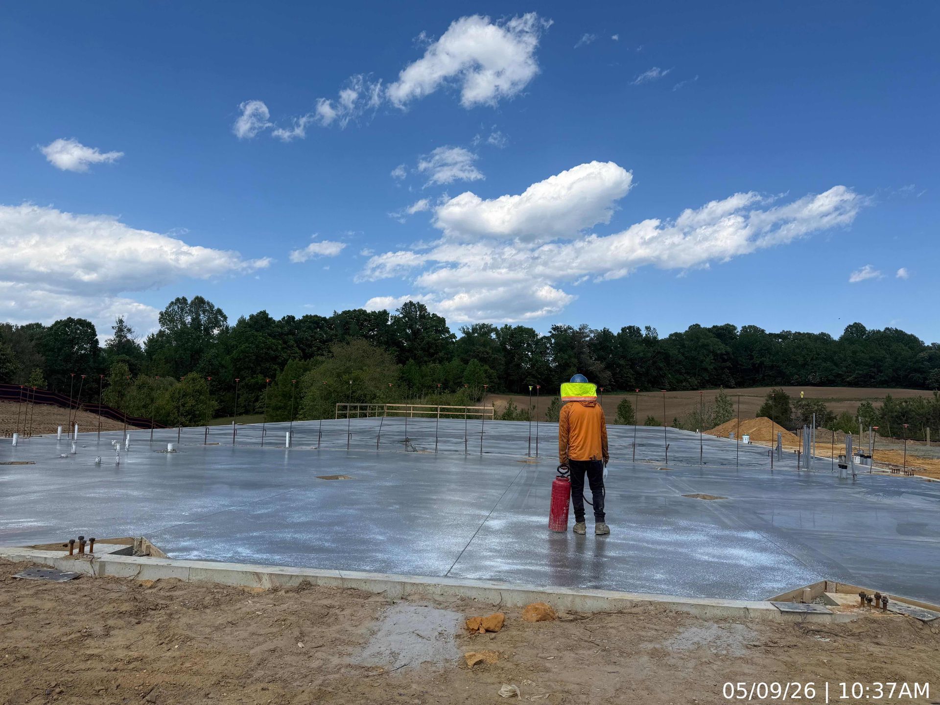 Worker in orange vest standing on a concrete slab at a construction site under a blue sky.
