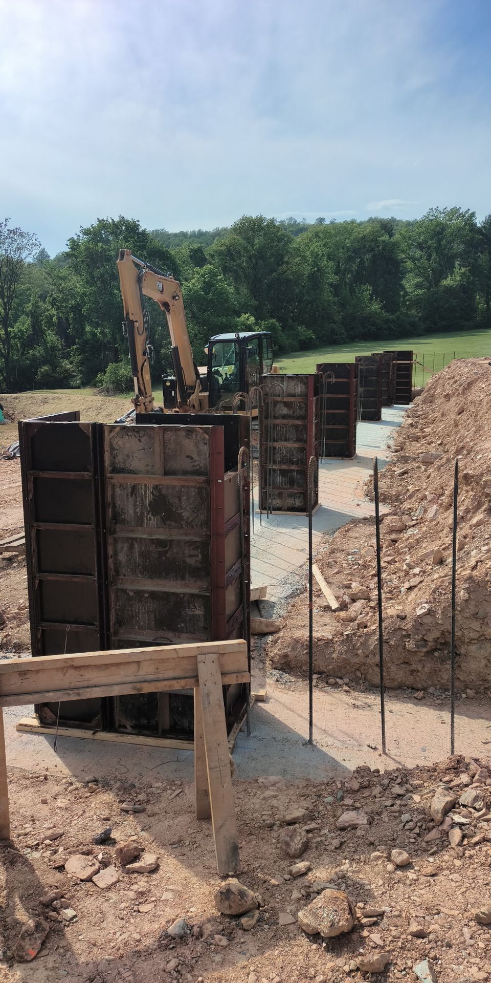 Construction site with excavator, formwork, and gravel trench in a wooded area