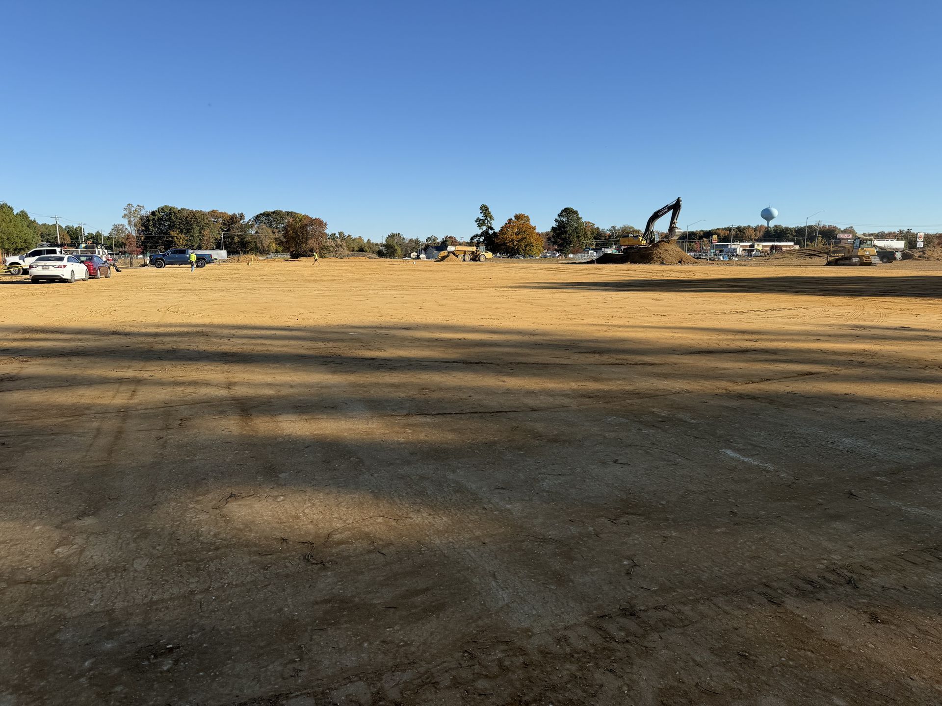 Wide dirt lot under a clear blue sky, with parked cars and construction equipment in the distance.