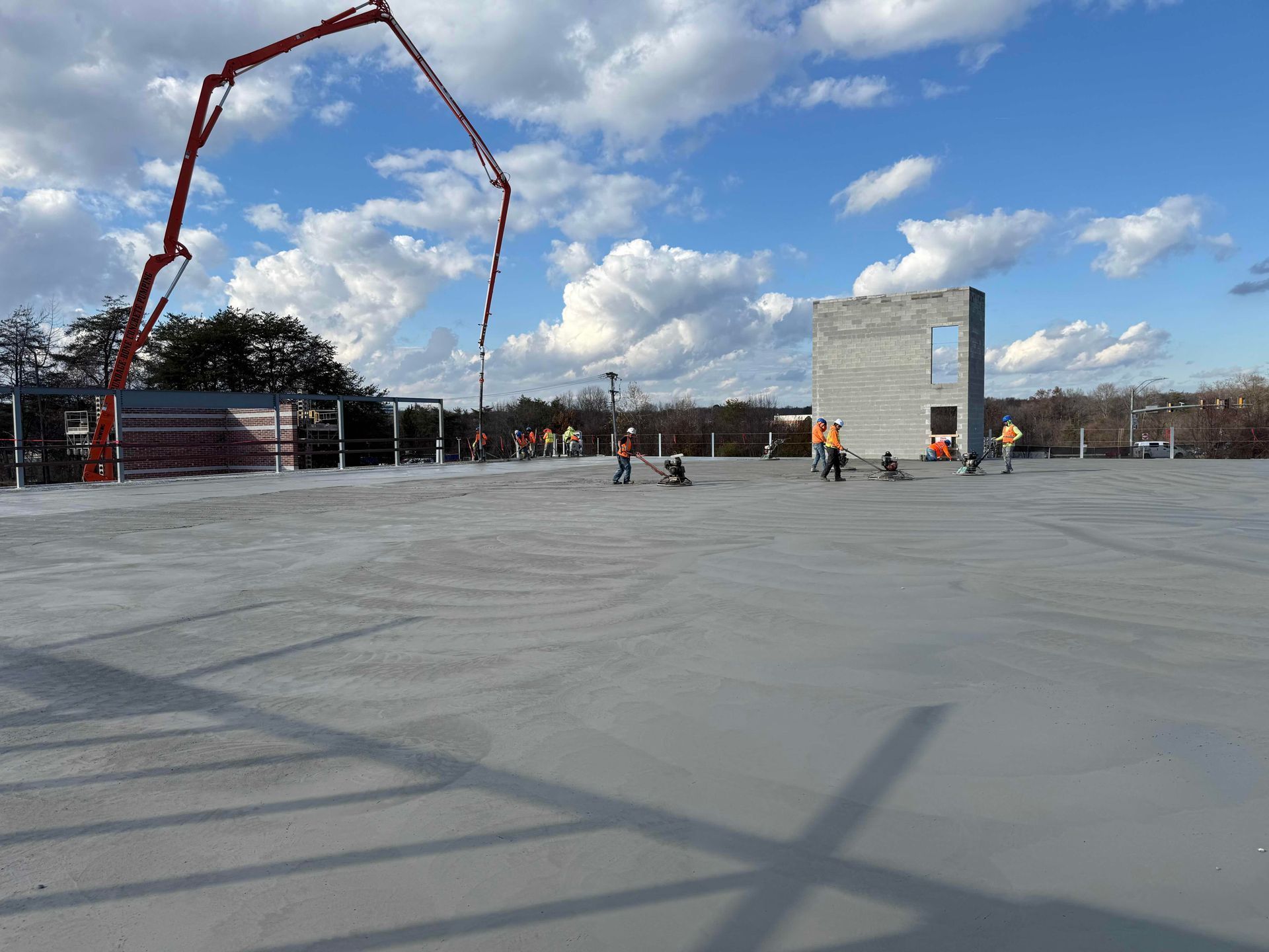 Concrete slab under construction with workers, a large crane arm, and a blue sky with clouds