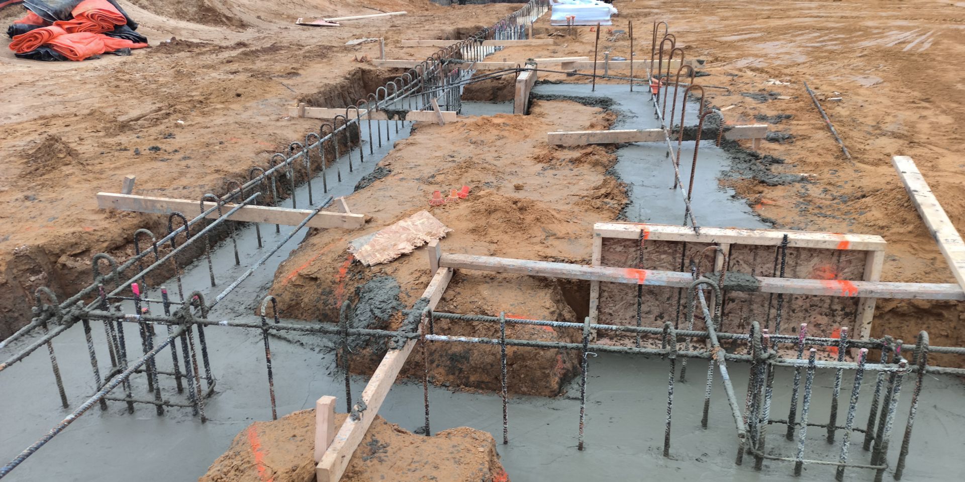 Foundation trenches with exposed rebar and wooden formwork at a construction site