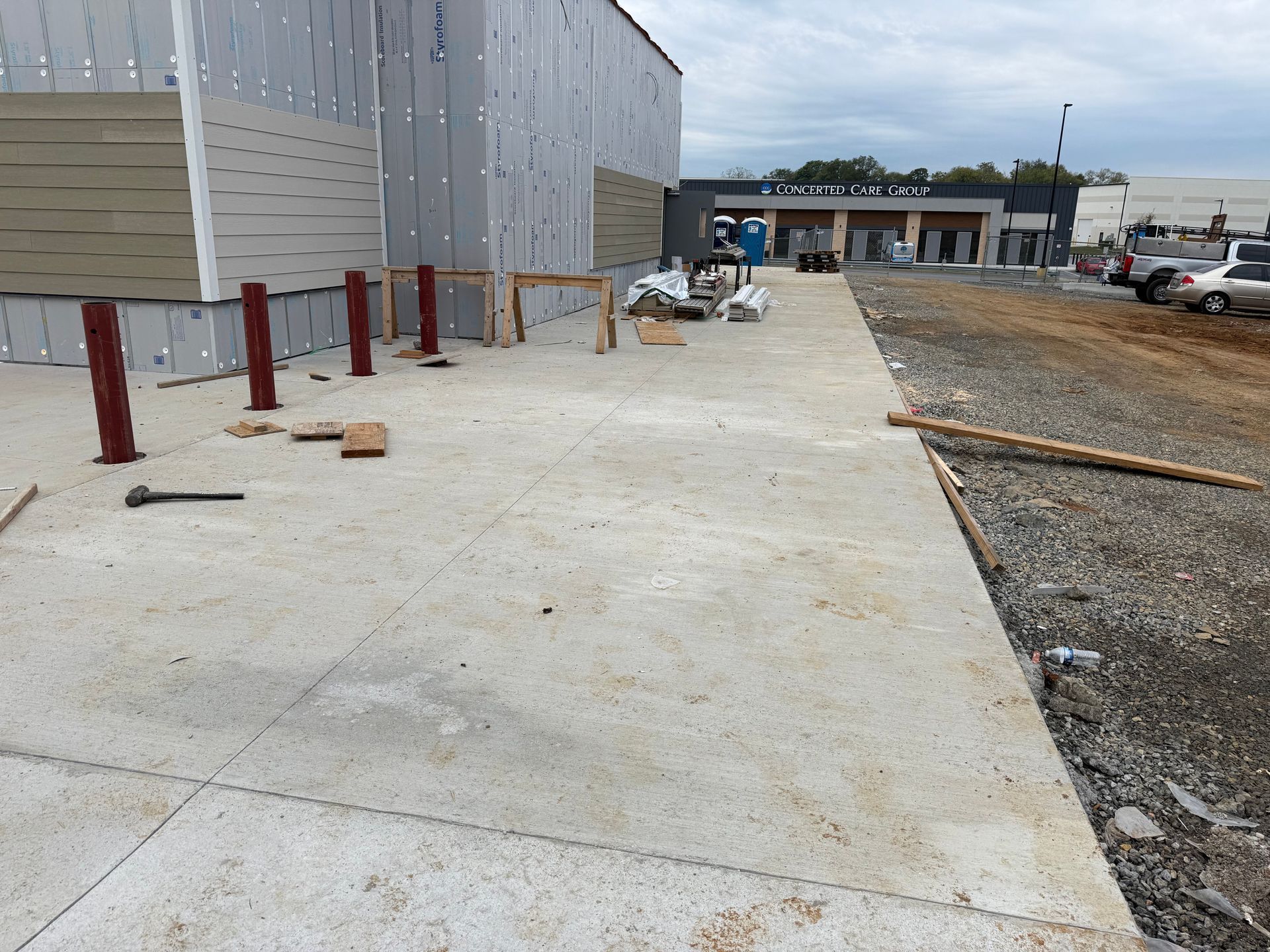 Concrete walkway beside a building under construction, with red bollards and scattered tools.