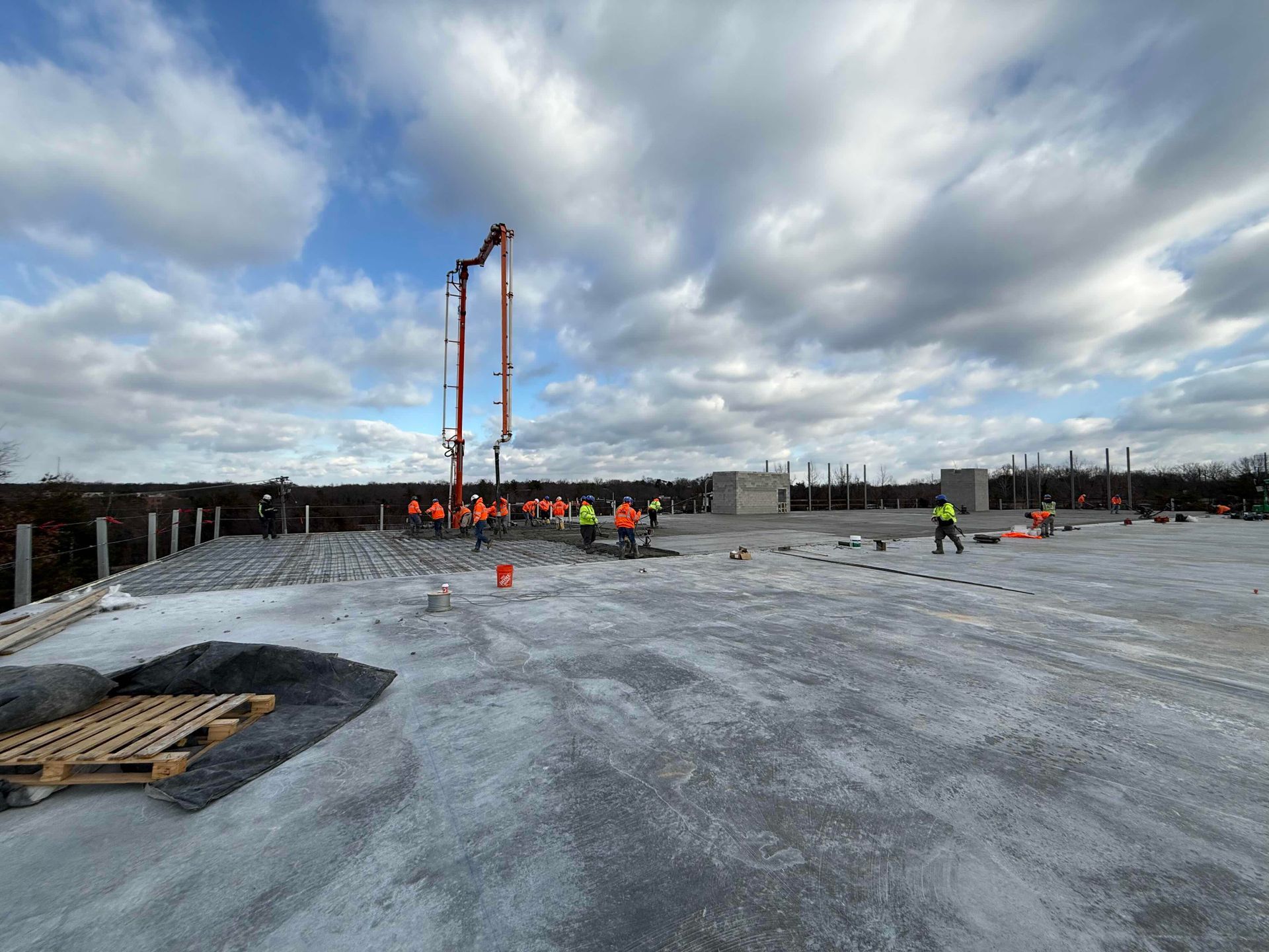 Construction workers on a concrete slab with a tall pump truck under cloudy sky