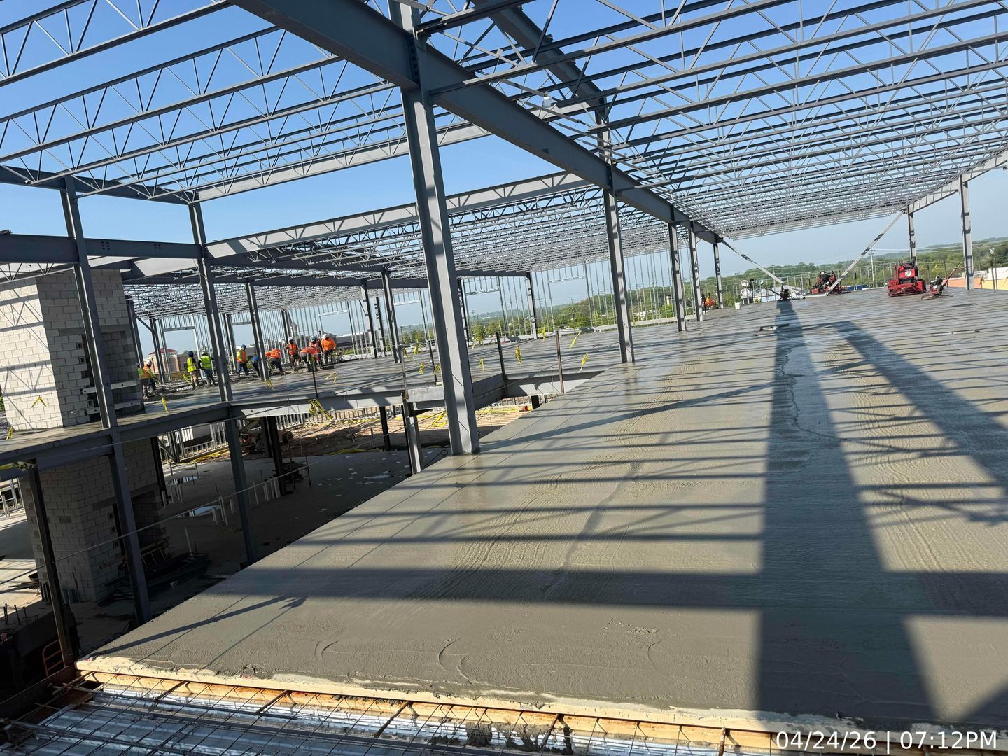 Large steel-framed building under construction with a concrete slab and open roof structure under clear sky