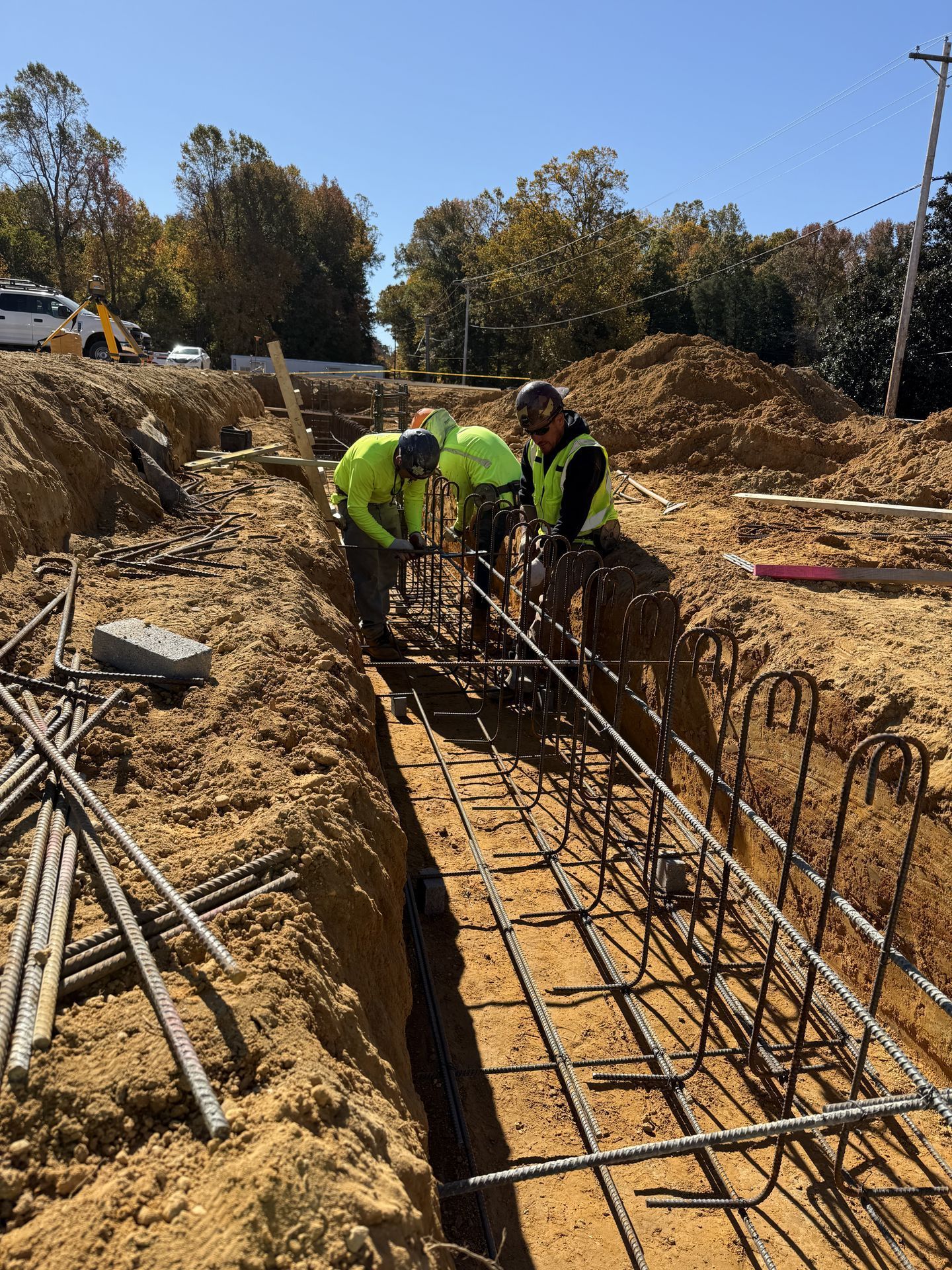 Workers in neon safety vests installing rebar in a deep trench at a construction site.