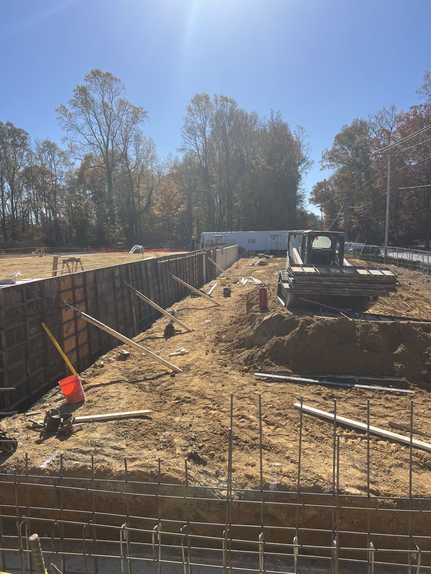 Construction site with excavator, trench, and exposed rebar under a clear blue sky