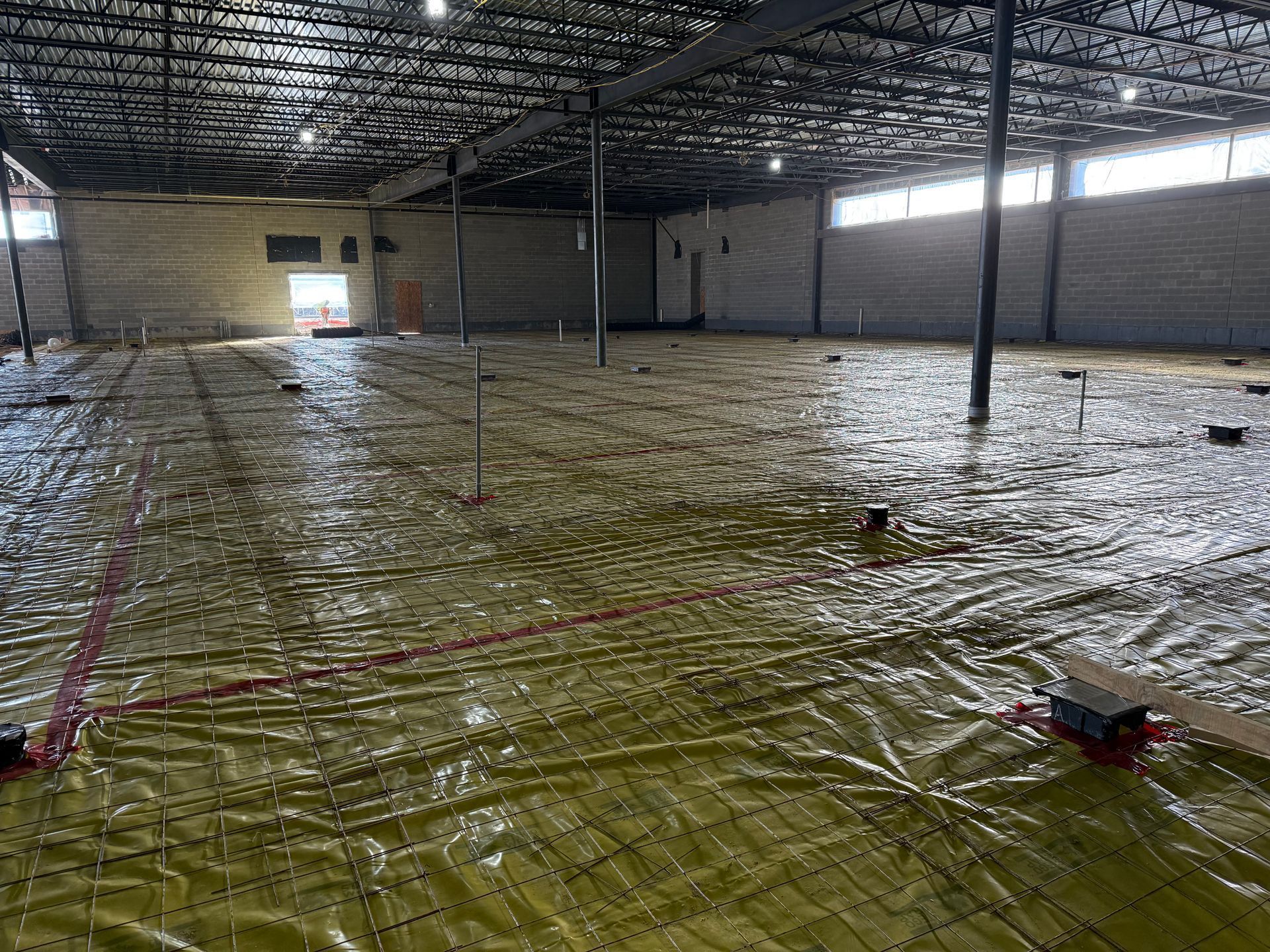 Large empty warehouse with a plastic-covered floor and columns under a high metal roof.