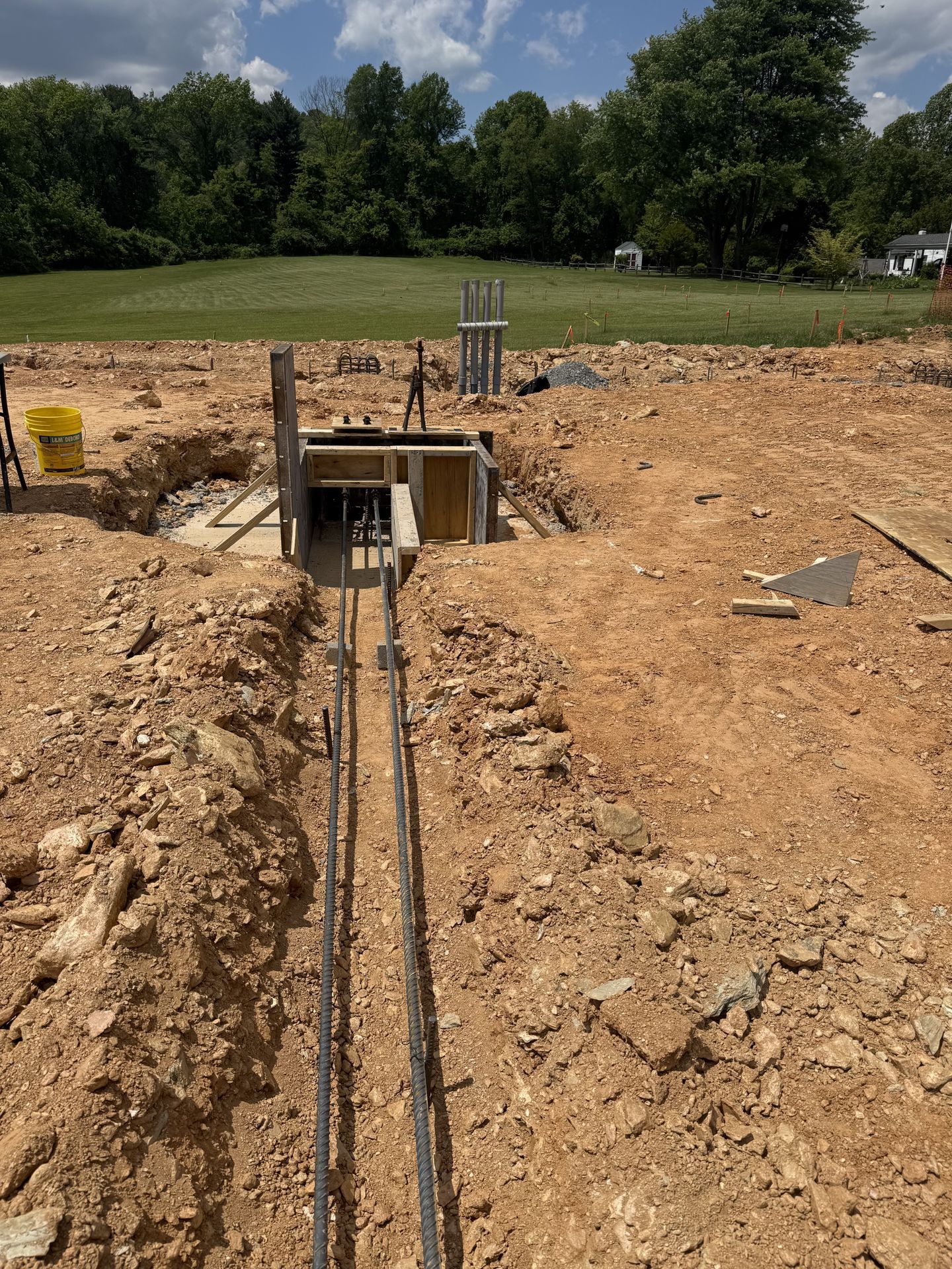 Trenched utility conduit leading to a concrete pit at a construction site under a cloudy sky