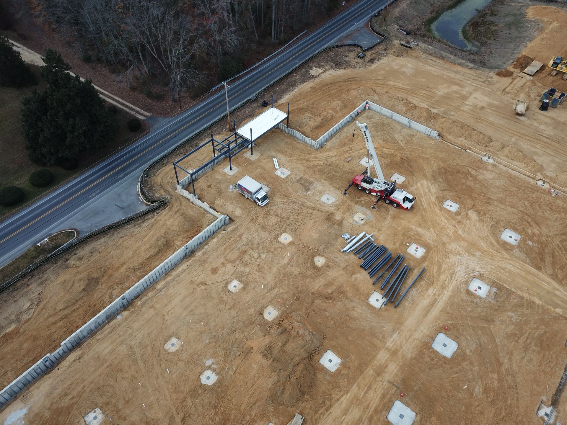 Aerial view of a construction site with a crane, concrete pads, and a road along the edge.