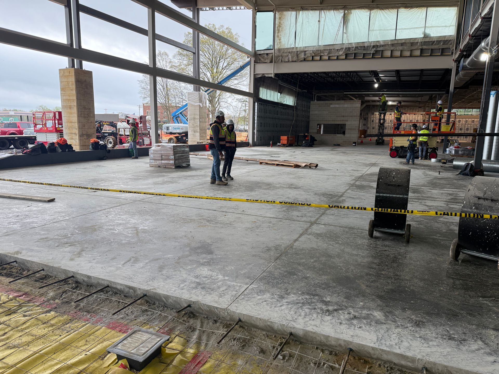 Construction site interior with two workers, concrete floor, and yellow caution tape.